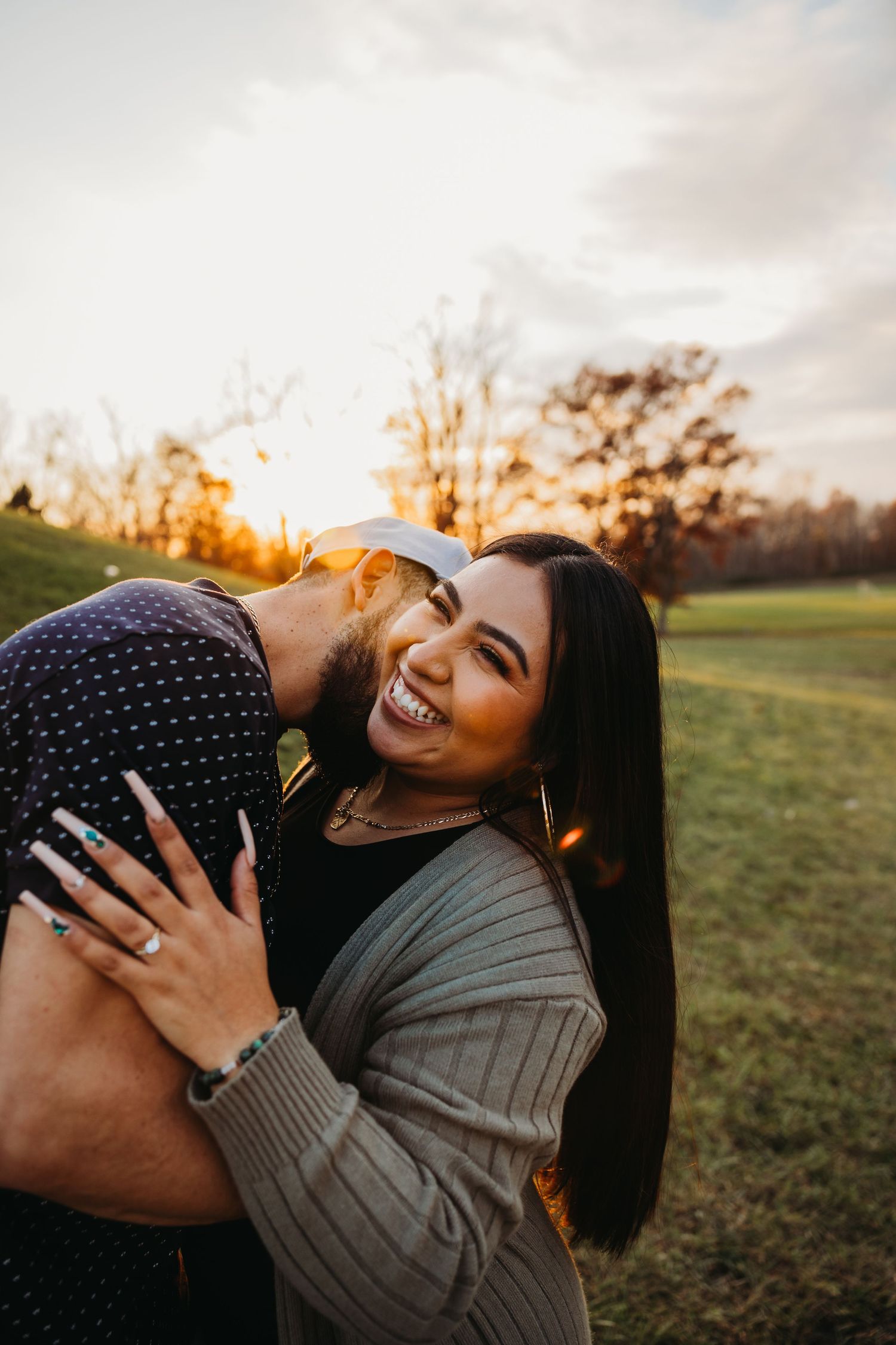 Happy couple laughing together outdoors during golden hour with trees in background.