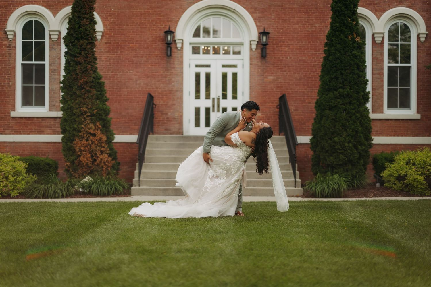 A romantic wedding photo captured in front of a historic red brick building with white columns and architectural details.