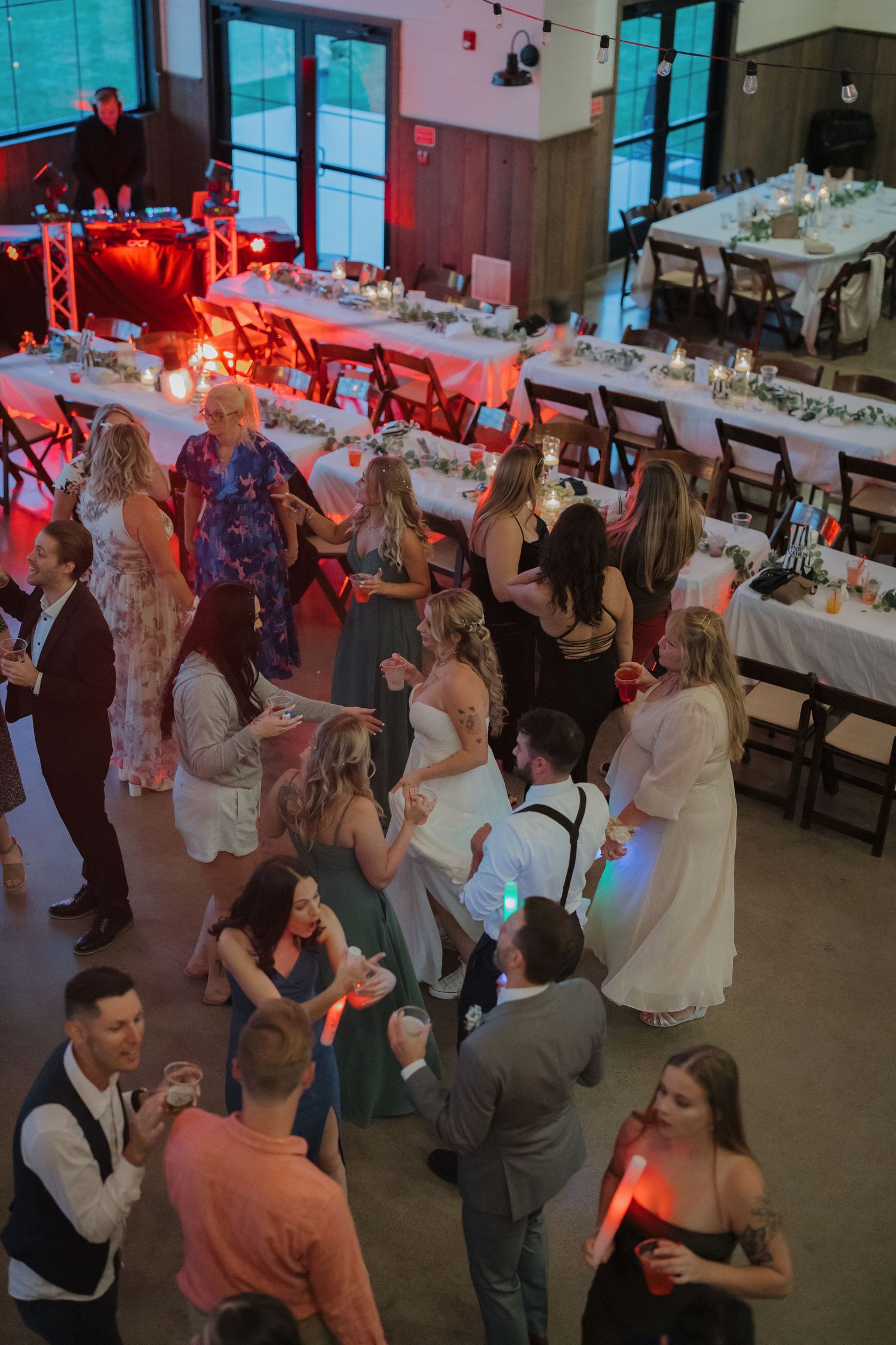 Wedding reception dance floor filled with guests under colorful lighting and string lights.