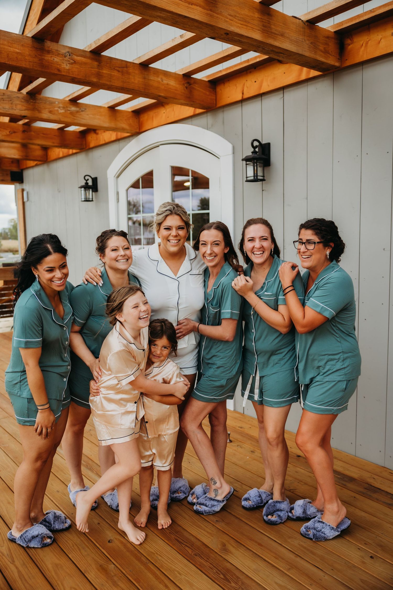 Wedding party in matching teal outfits posing on wooden deck.