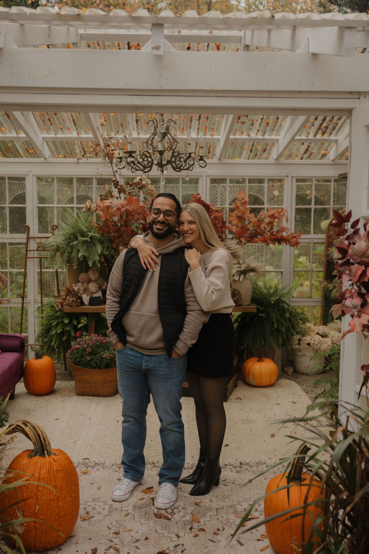A cozy autumn scene with pumpkins and plants decorating a white greenhouse or sunroom interior.