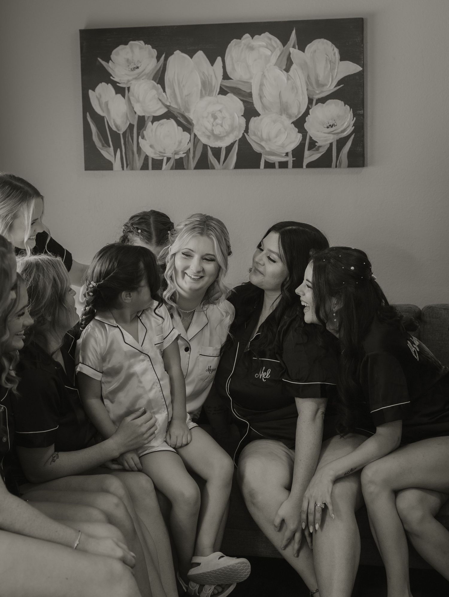 Black and white photo of wedding party relaxing on couch under floral wall art.