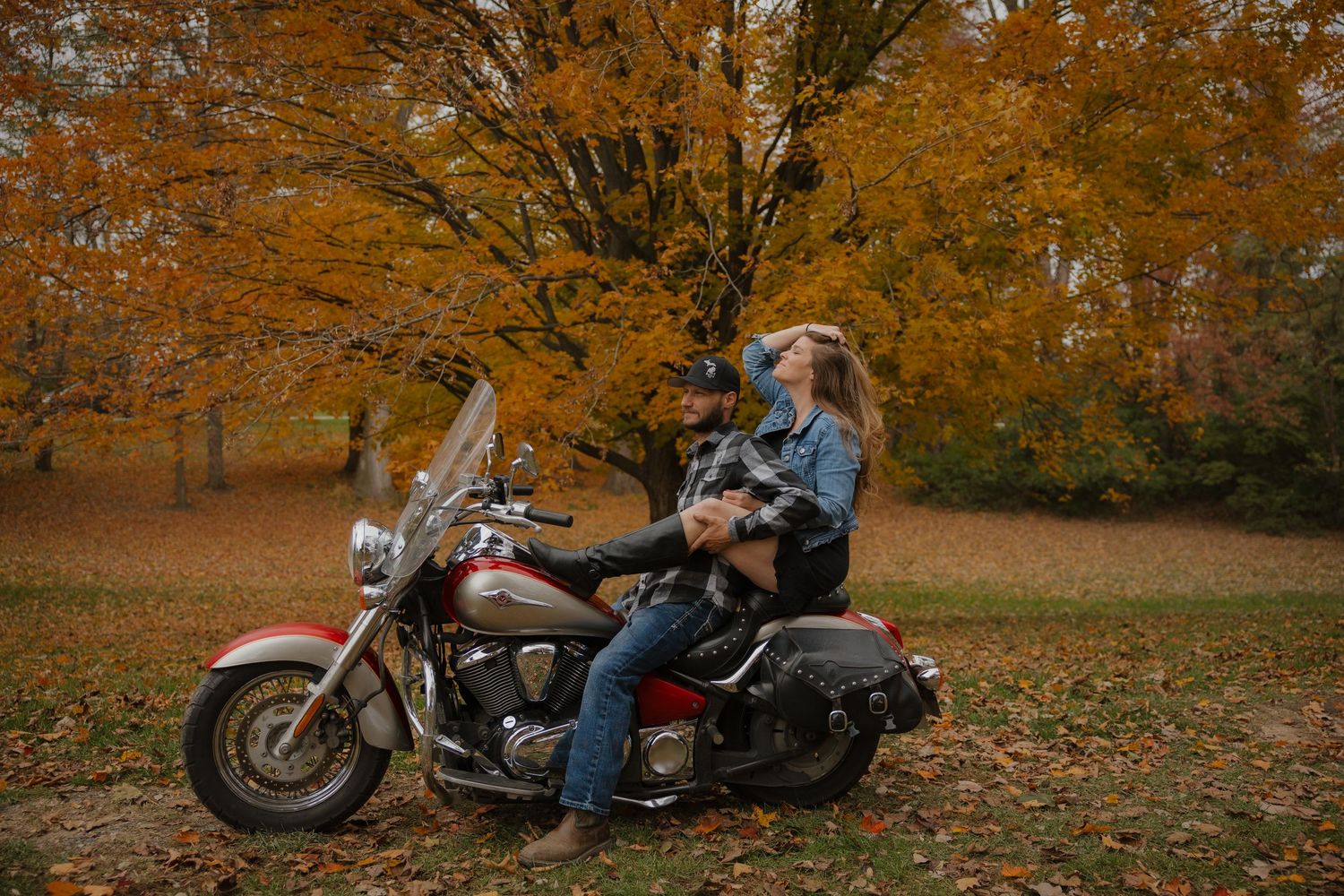 A motorcycle rider sits on a parked bike surrounded by vibrant autumn foliage in a forest setting.