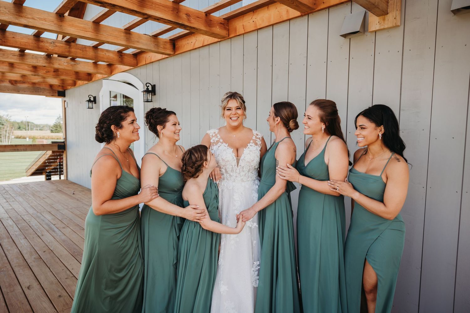 Bride in white dress surrounded by bridesmaids in teal dresses on outdoor deck.