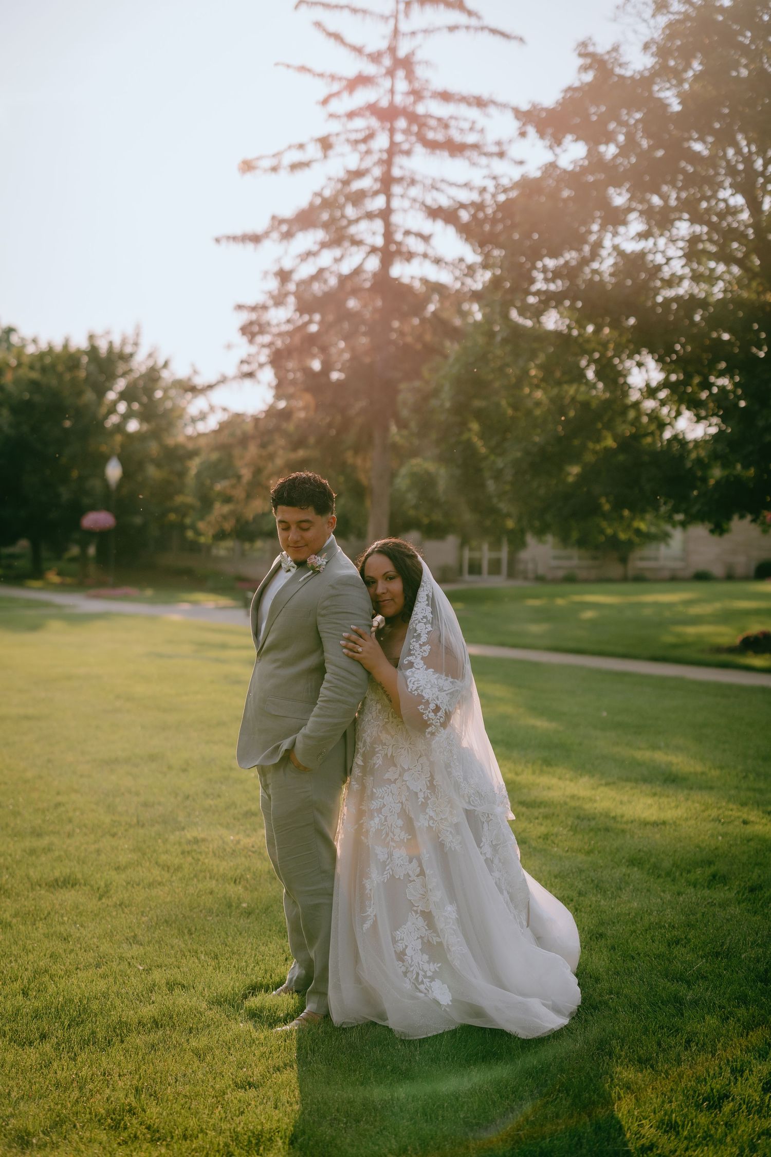 A newlywed couple embraces on a sunlit lawn during sunset at their outdoor wedding ceremony.