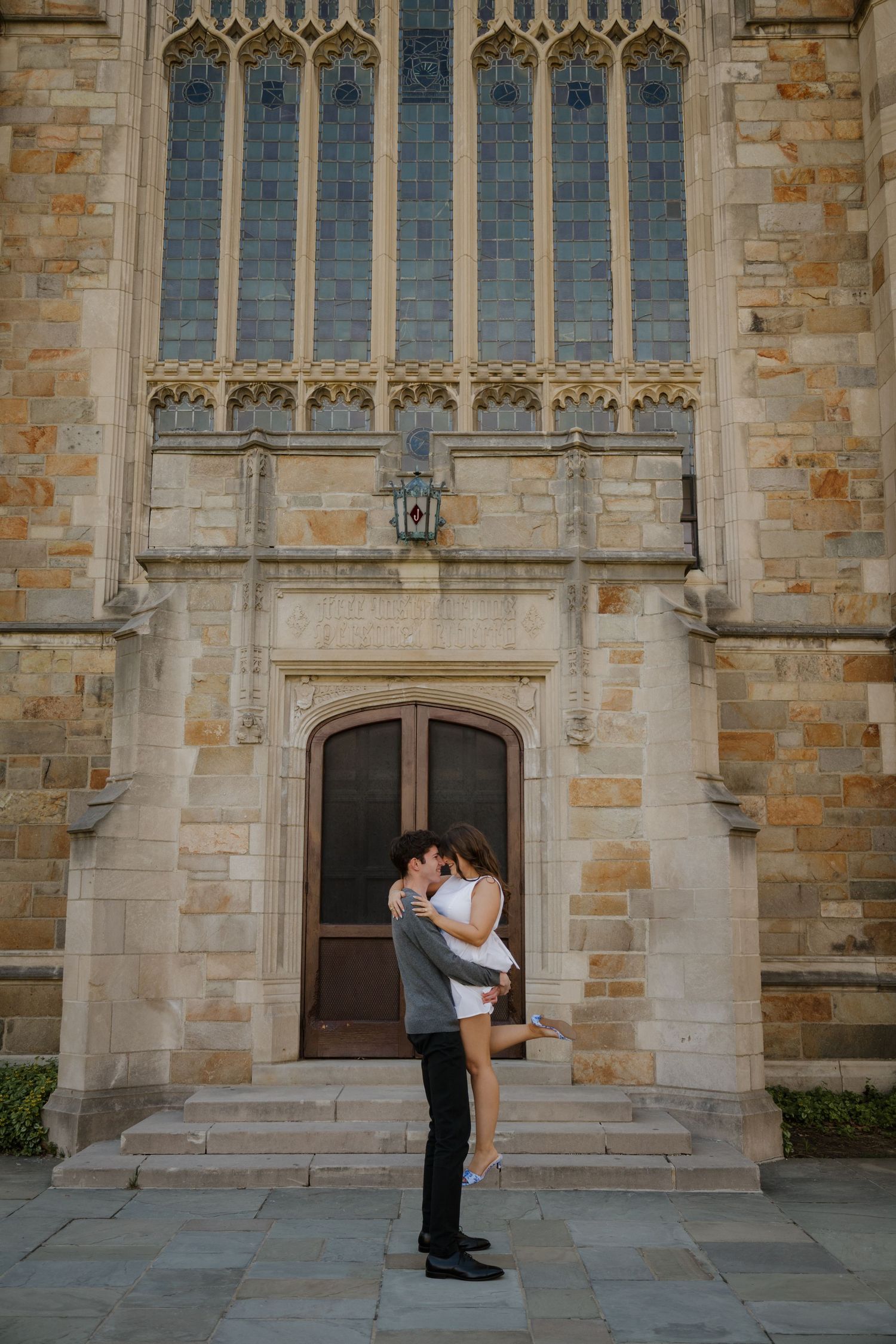 Couple sharing a romantic kiss in front of a Gothic stone church entrance with ornate stained glass windows.