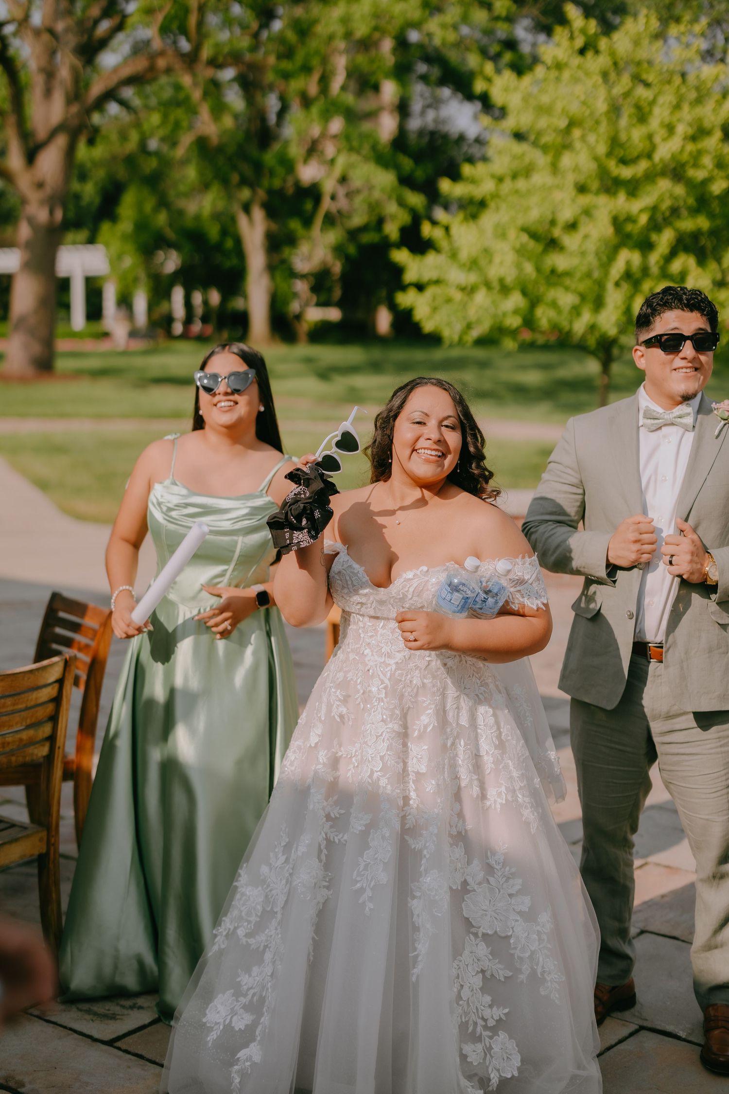 Wedding party members share a joyful moment outdoors as they walk together in formal attire on a sunny day.