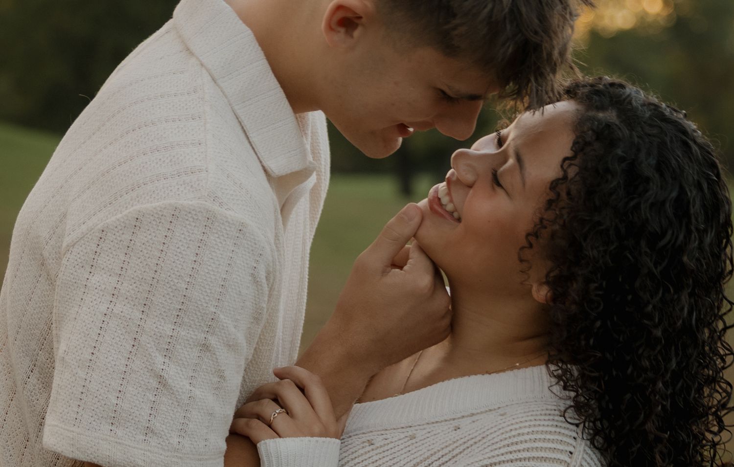 A romantic couple in white attire shares an intimate moment outdoors during a golden sunset.
