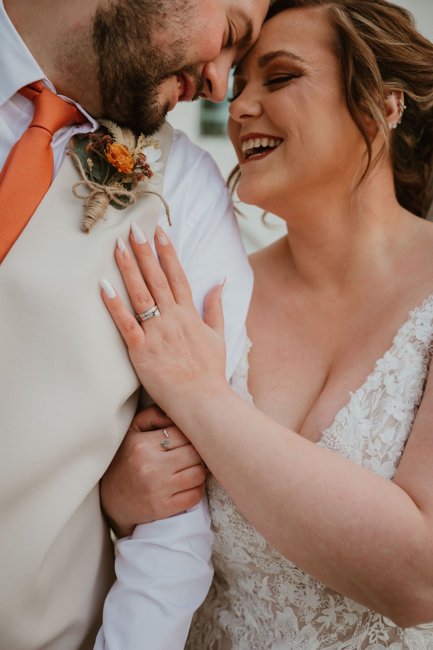 Close-up shot of a joyful bride and groom sharing an intimate moment with the groom wearing a distinctive orange boutonniere.