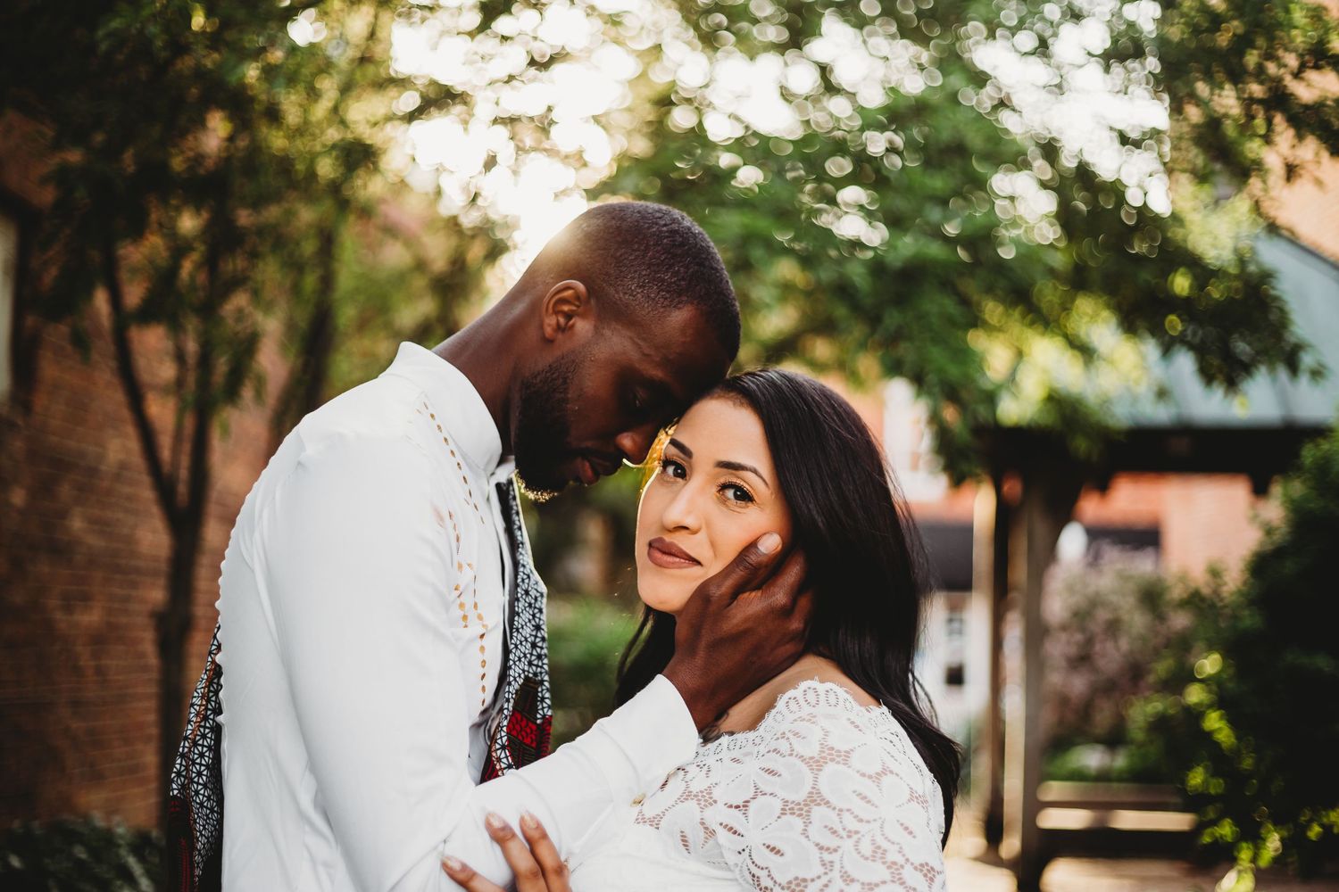 A romantic couple in wedding attire embraces outdoors during a golden sunset photoshoot.