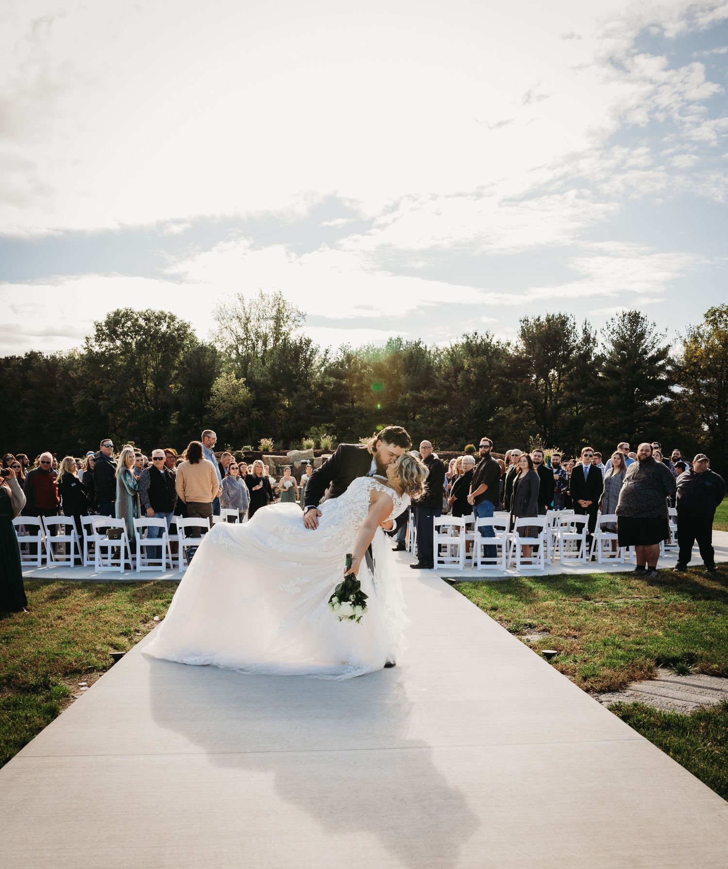 Couple sharing romantic moment on white aisle runner during outdoor wedding ceremony.
