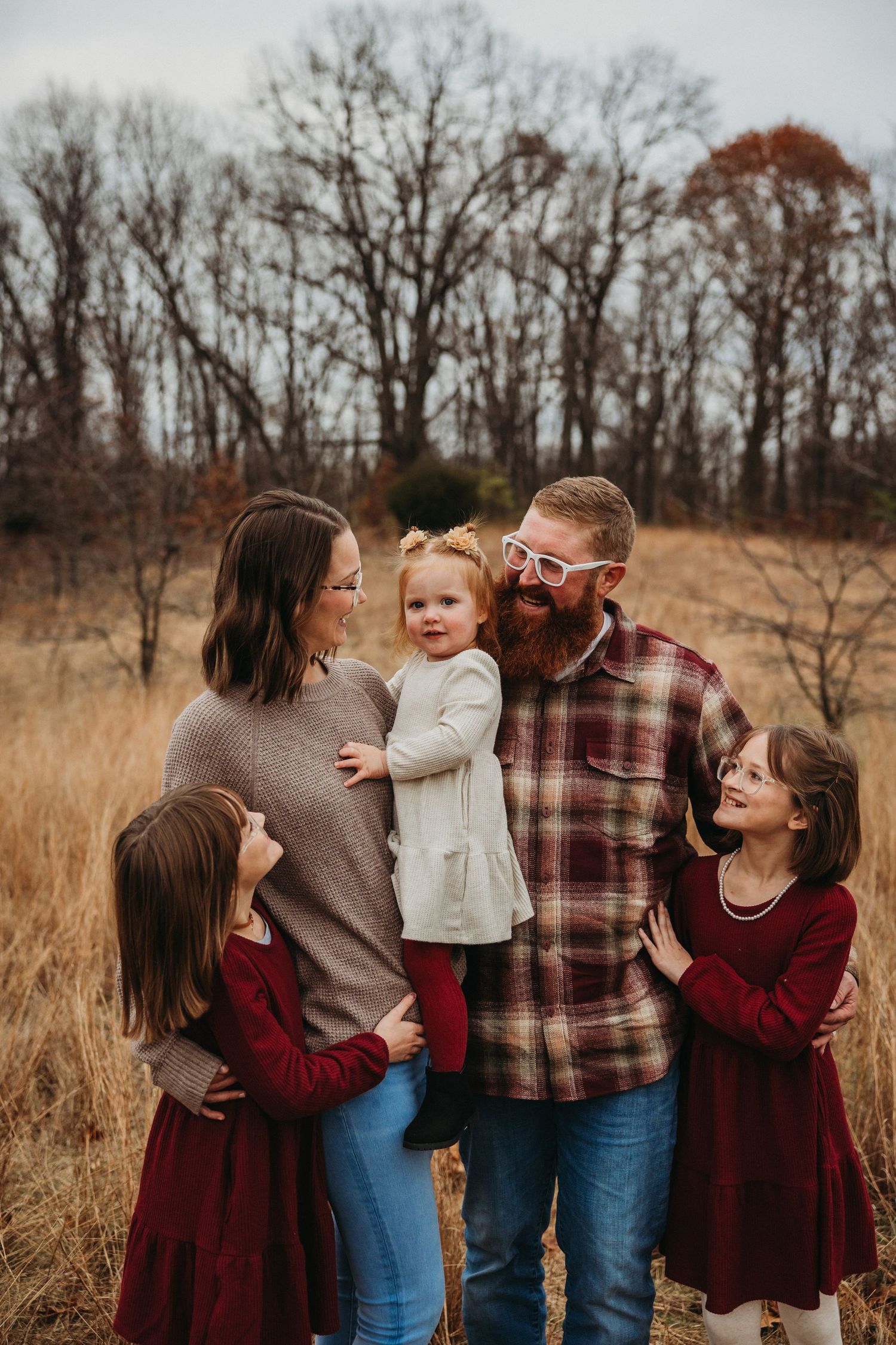 Family in coordinating burgundy outfits sharing playful moments in a fall field.