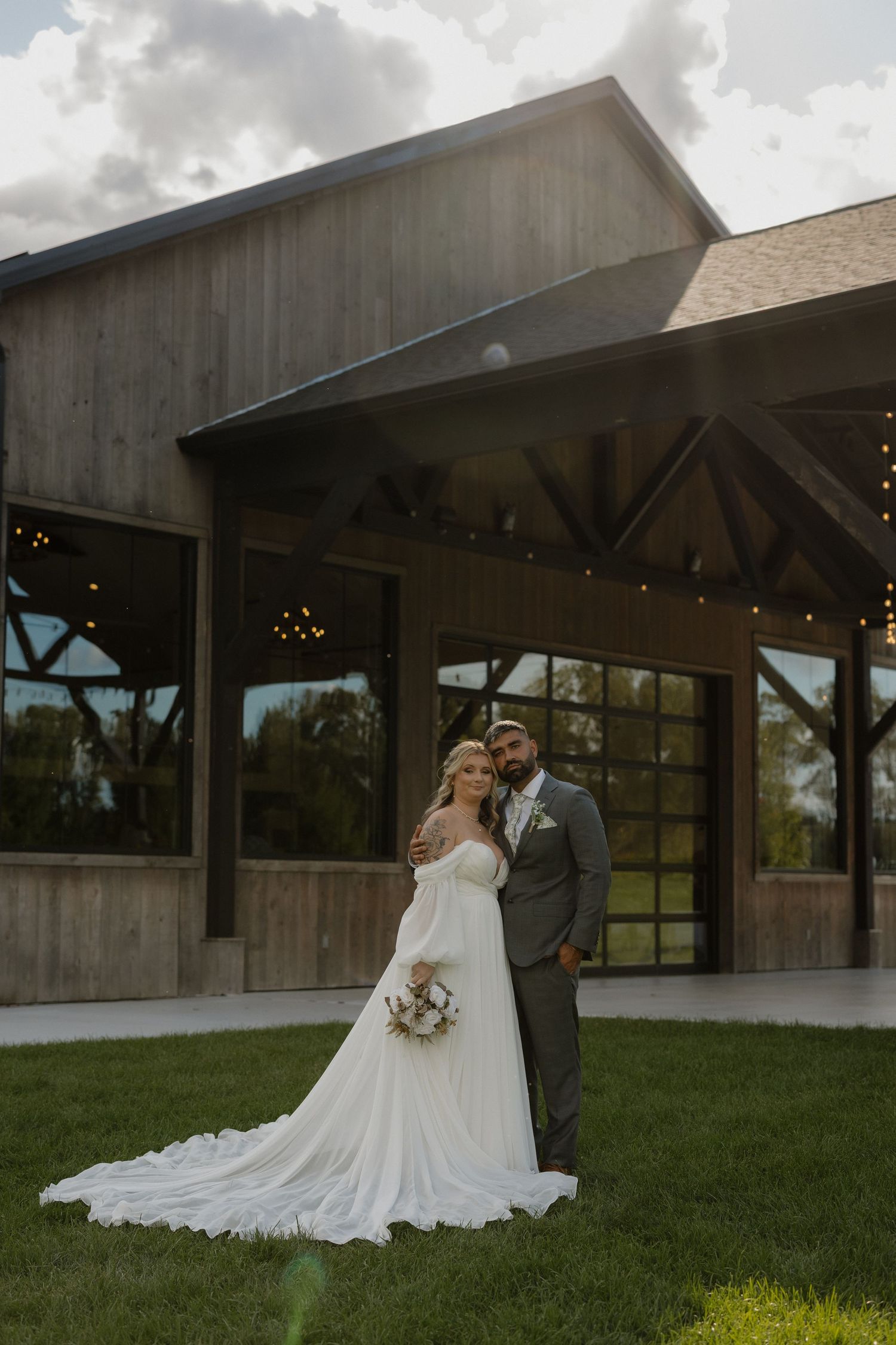 Romantic wedding portraits outside modern rustic venue with flowing white dress and gray suit.