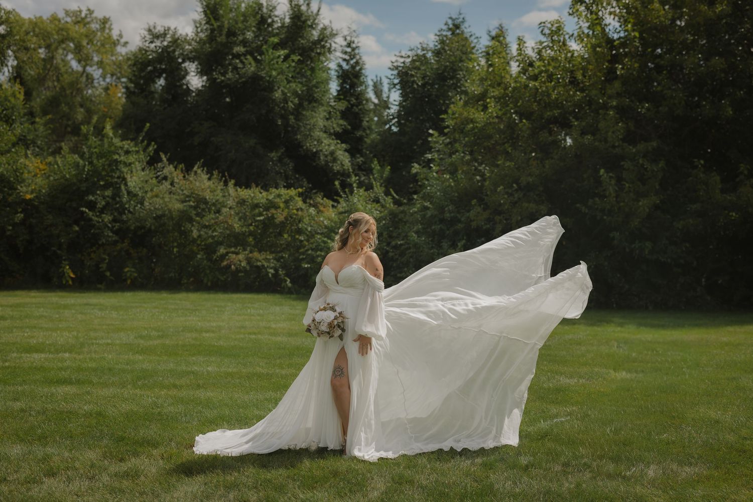 White wedding dress flowing dramatically in the wind on a green lawn.
