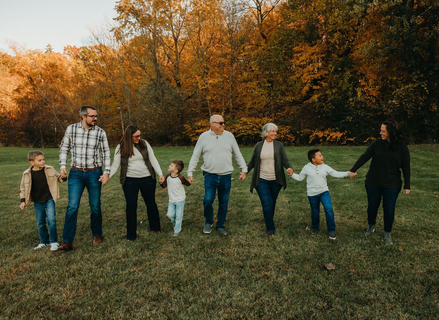 Group of people holding hands in line against autumn trees during golden hour.