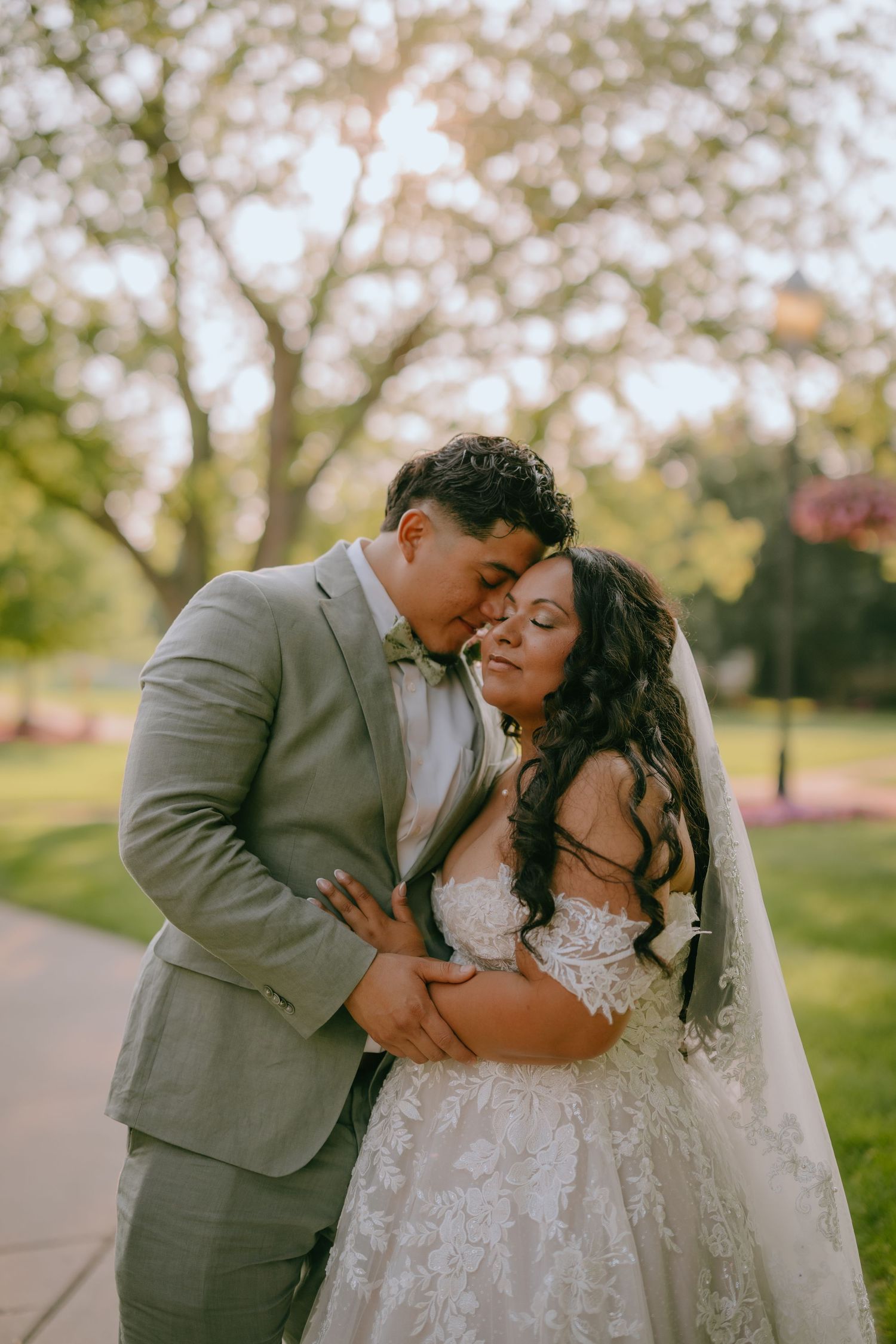 A joyful wedding couple embraces outdoors in a garden setting with soft bokeh lighting during their special day.