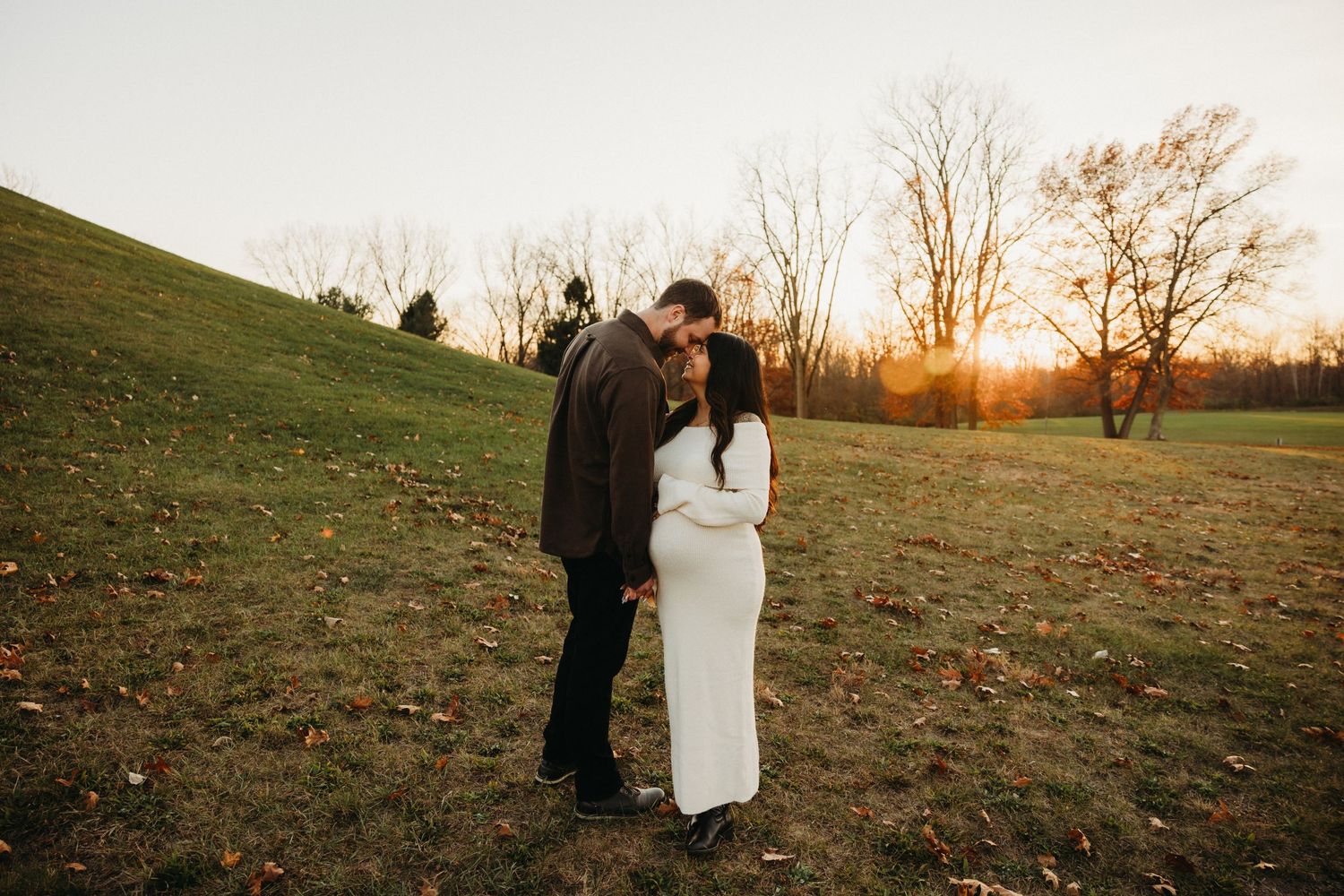 Couple in autumn field at sunset with woman in white dress and man in dark jacket.