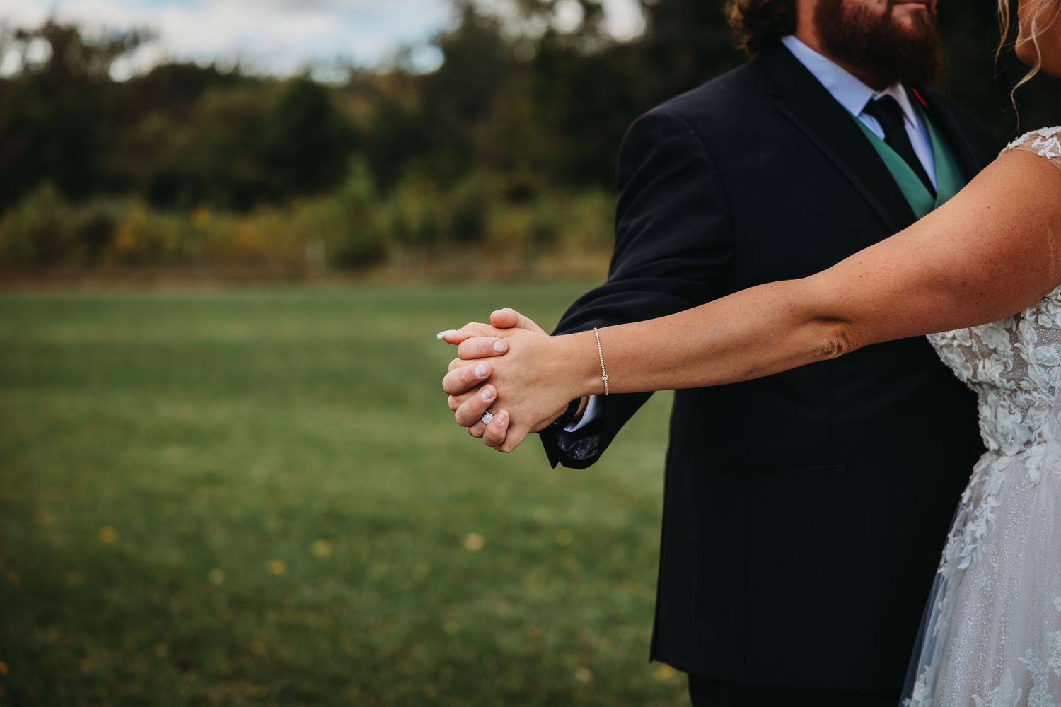 Close-up of newlyweds holding hands during outdoor wedding ceremony.