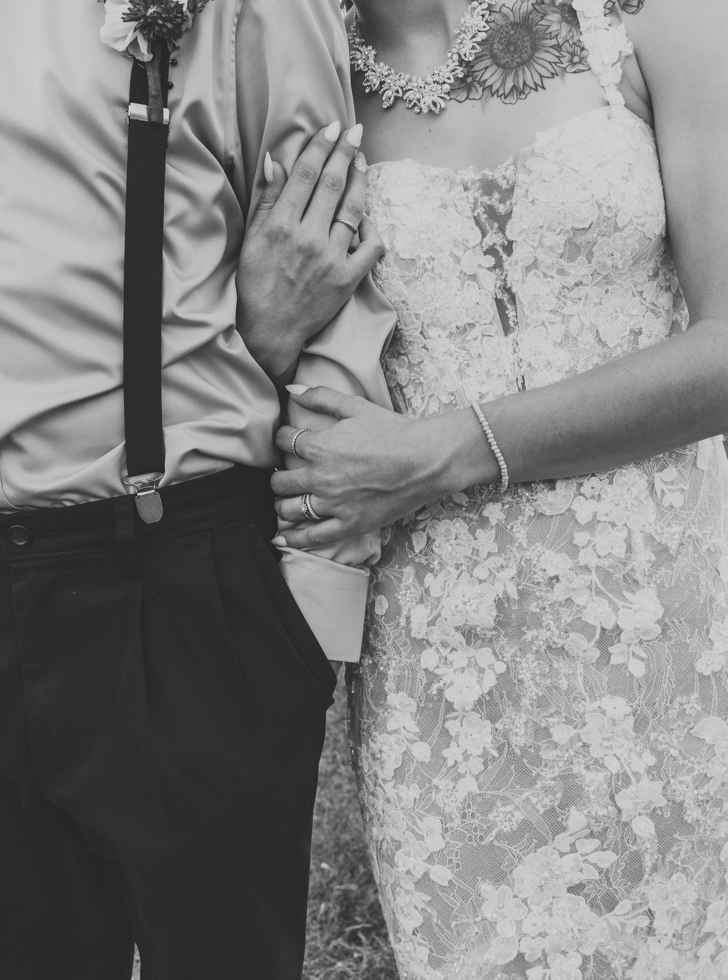 A black and white detail shot of a bride and groom showing wedding attire and ring.