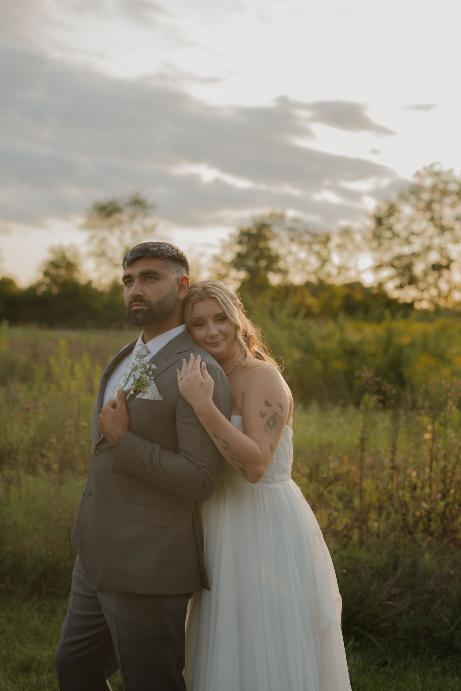 Sunset portrait of newlyweds embracing in field with golden light and natural landscape.