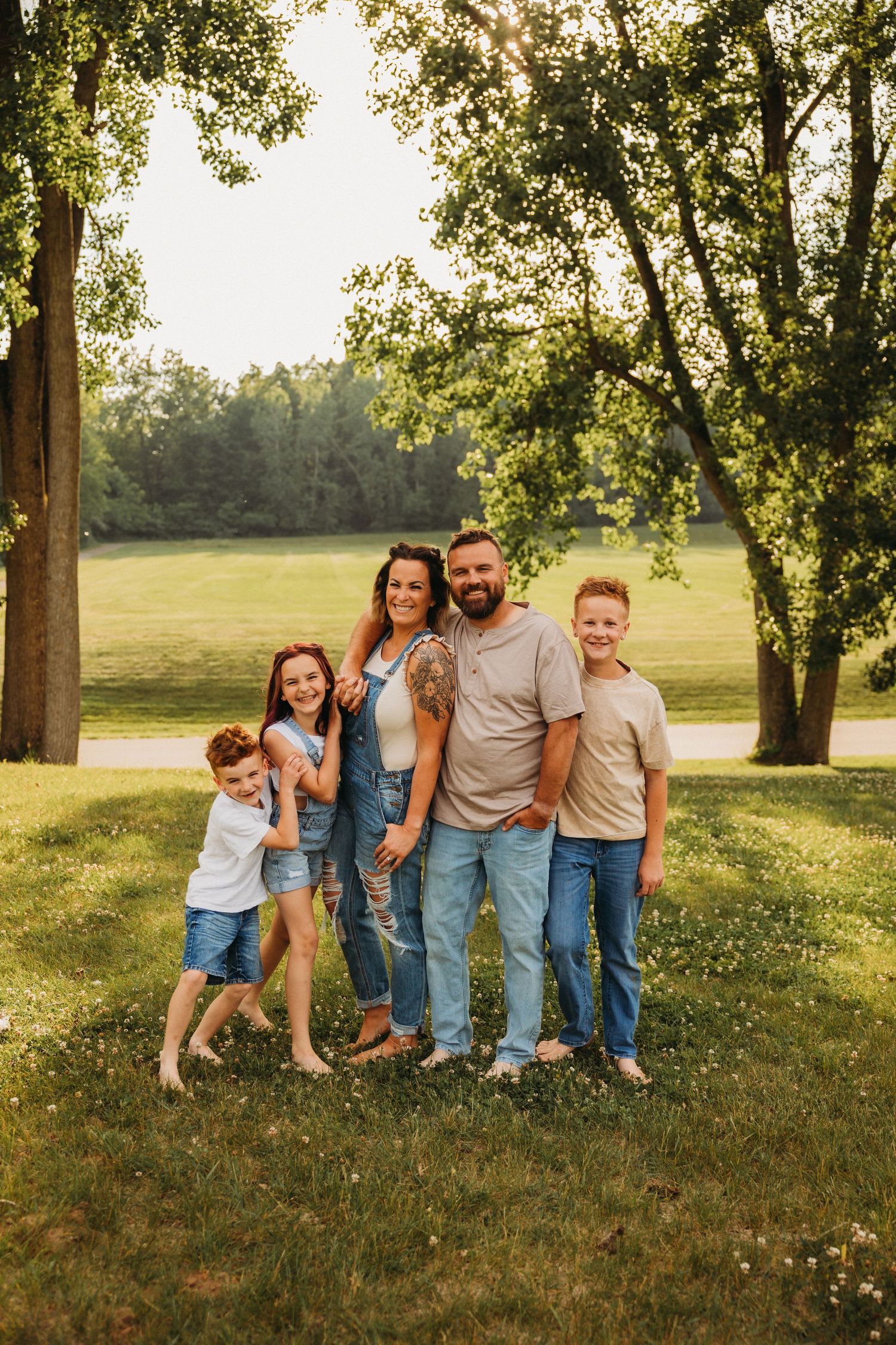 Group poses together on sunny grass field with tall trees casting dappled shadows.