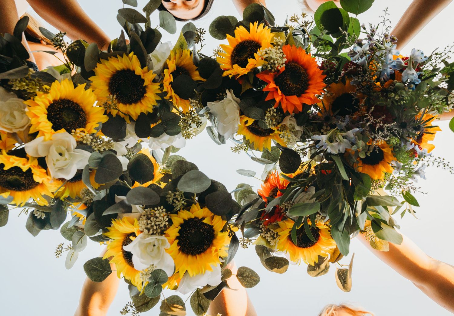 Bright sunflowers and greenery form a stunning wedding bouquet held by multiple hands.