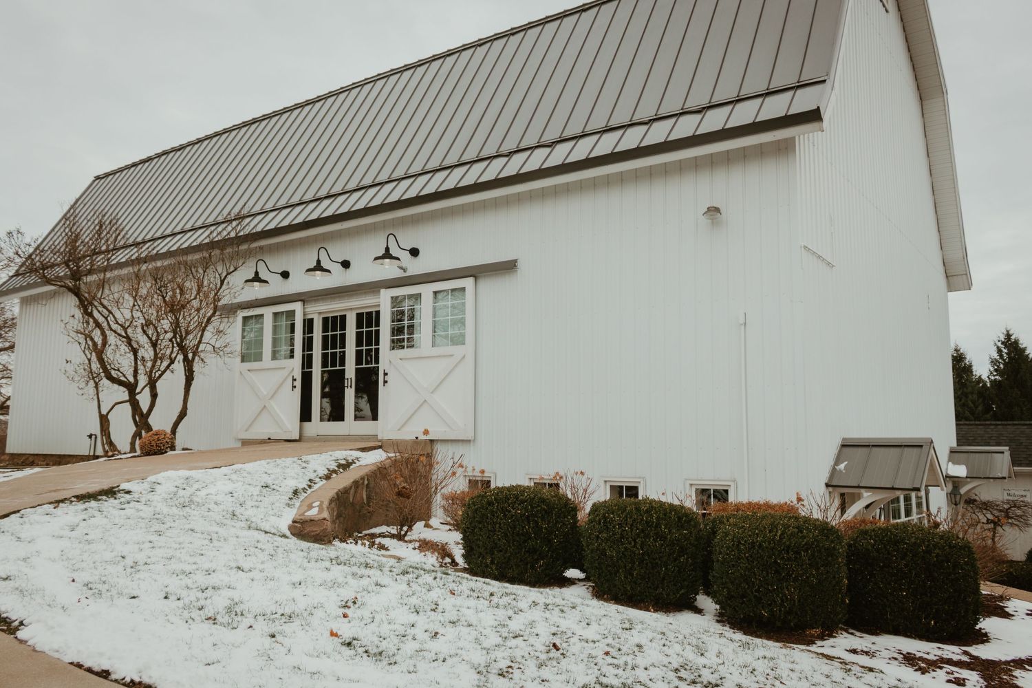 Modern white barn wedding venue with metal roof and landscaping in winter snow.