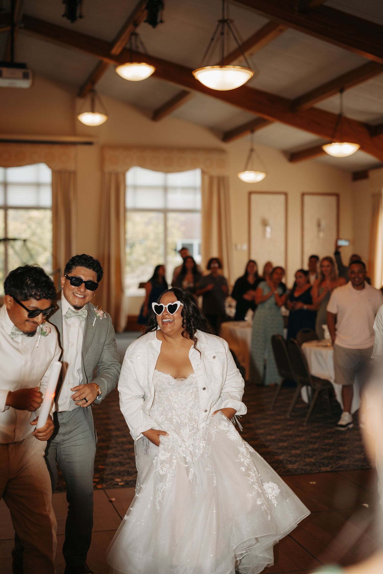 Wedding reception dance party scene with guests in sunglasses enjoying themselves under warm pendant lighting.