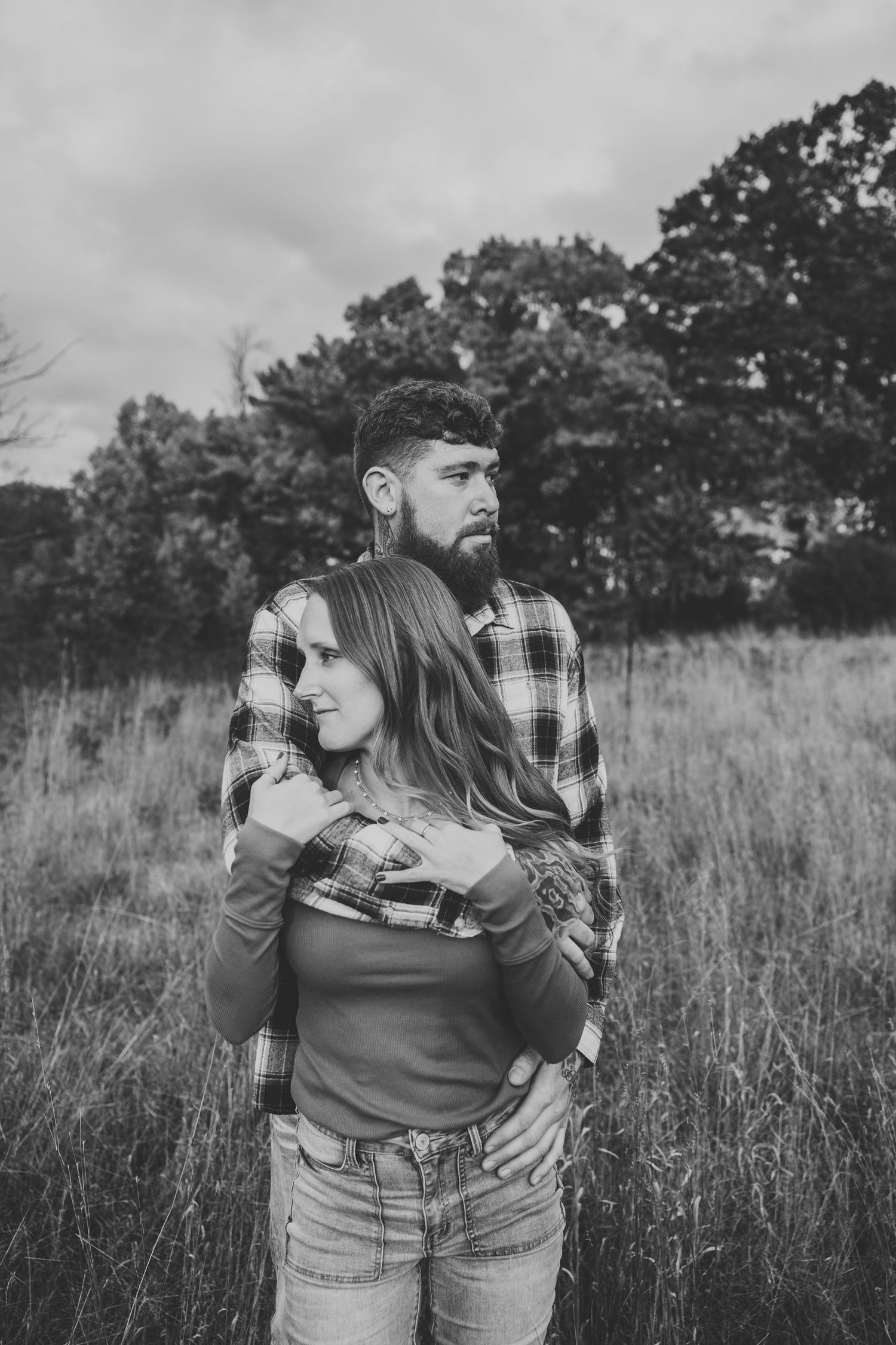 Black and white portrait of couple embracing in rustic field setting.