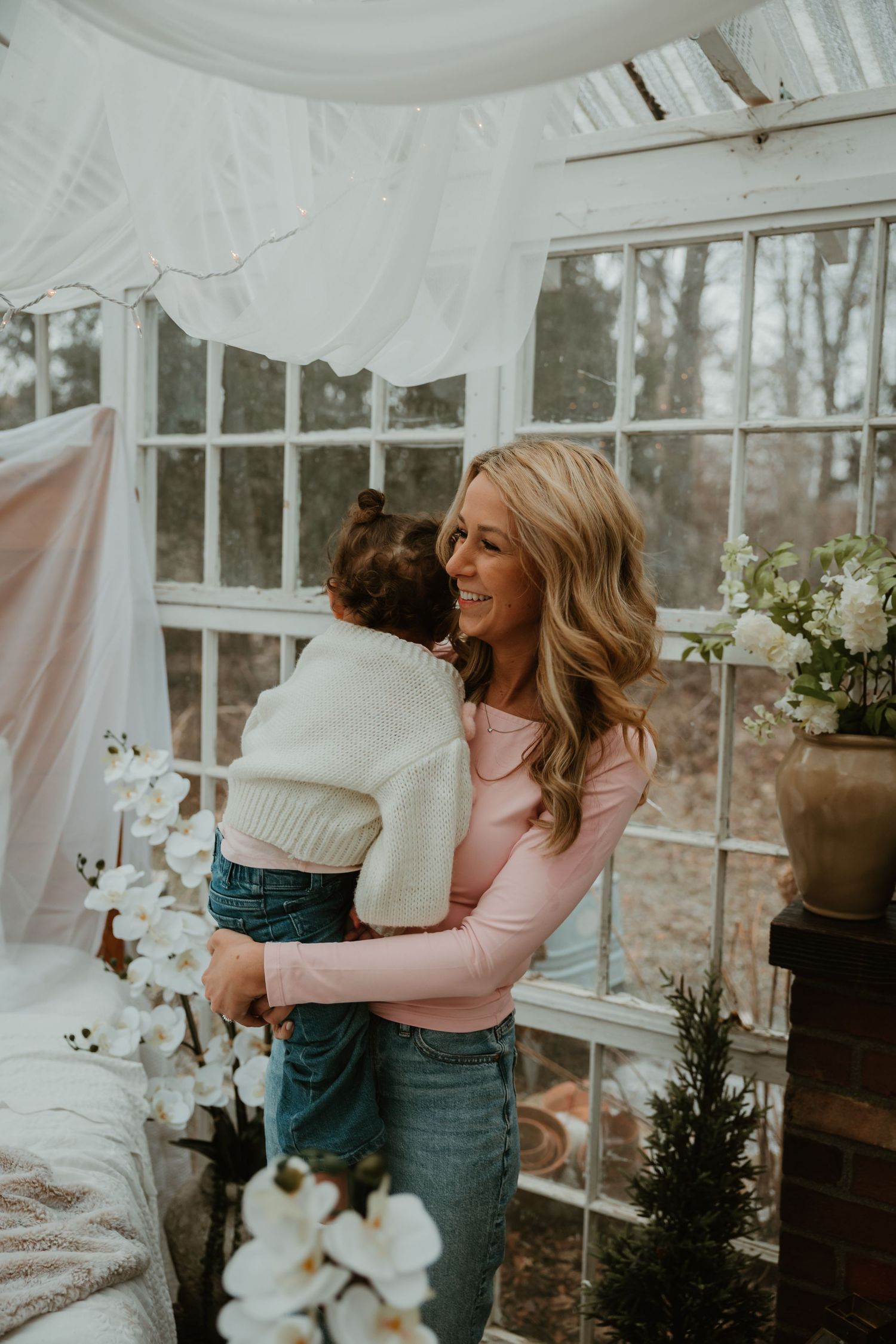 A joyful moment shared in a bright sunroom decorated with white drapes and potted flowers.