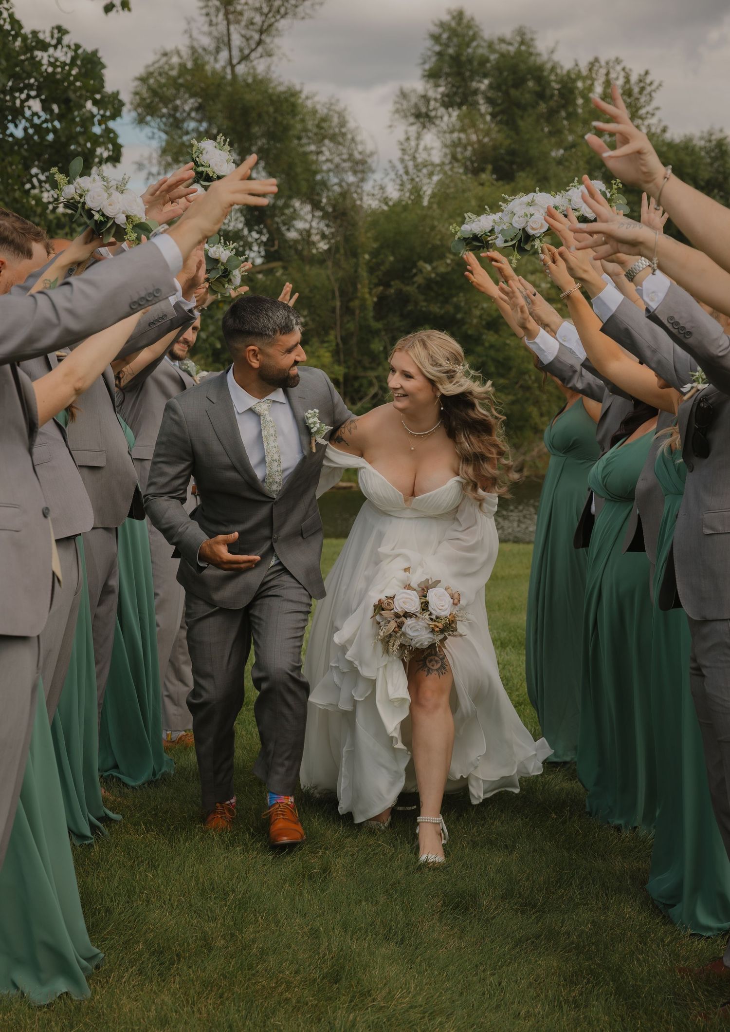 Wedding group performs synchronized jumping pose outdoors with bridesmaids in green and groomsmen in gray.