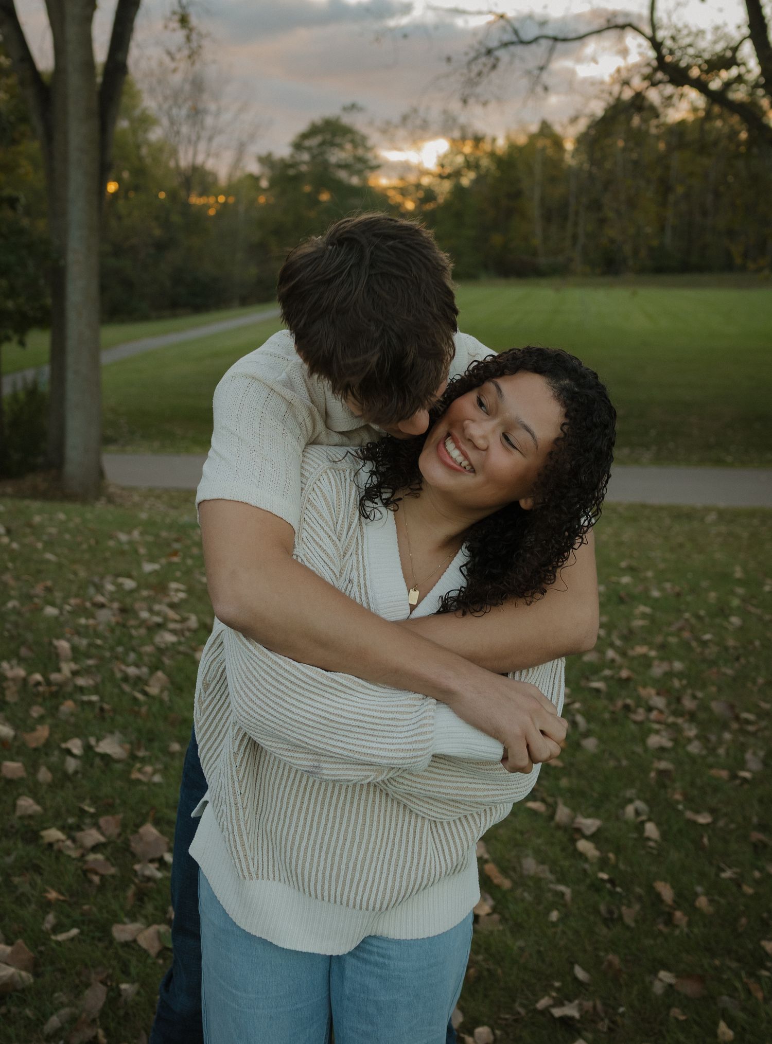 Two people embrace lovingly while standing in a park during autumn.