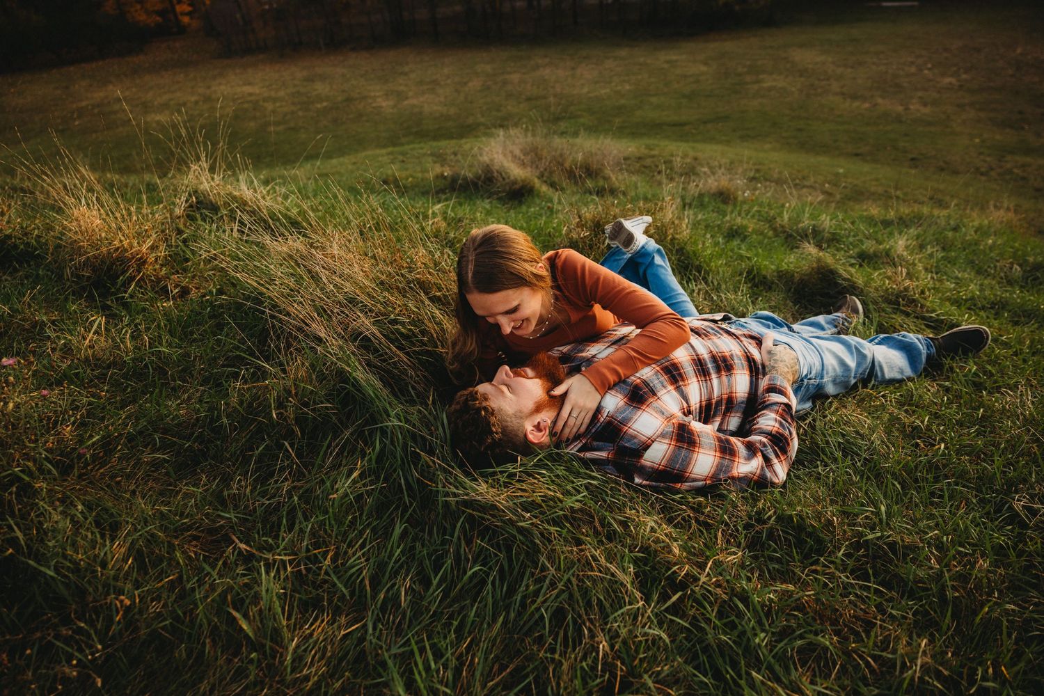 Couple laying in grass field sharing playful romantic moment at sunset.