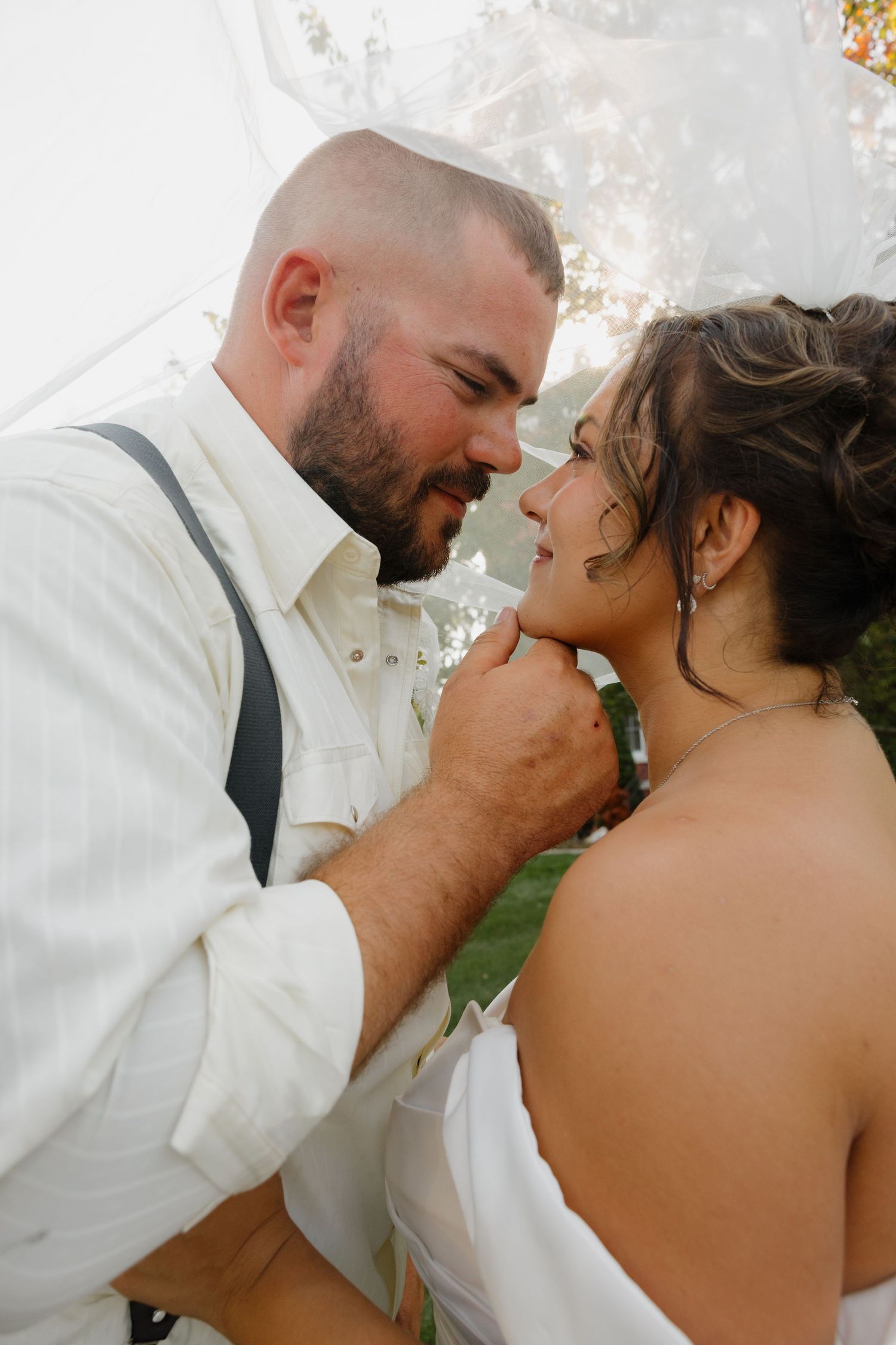A groom tenderly holds his bride's chin during an intimate outdoor wedding ceremony moment.