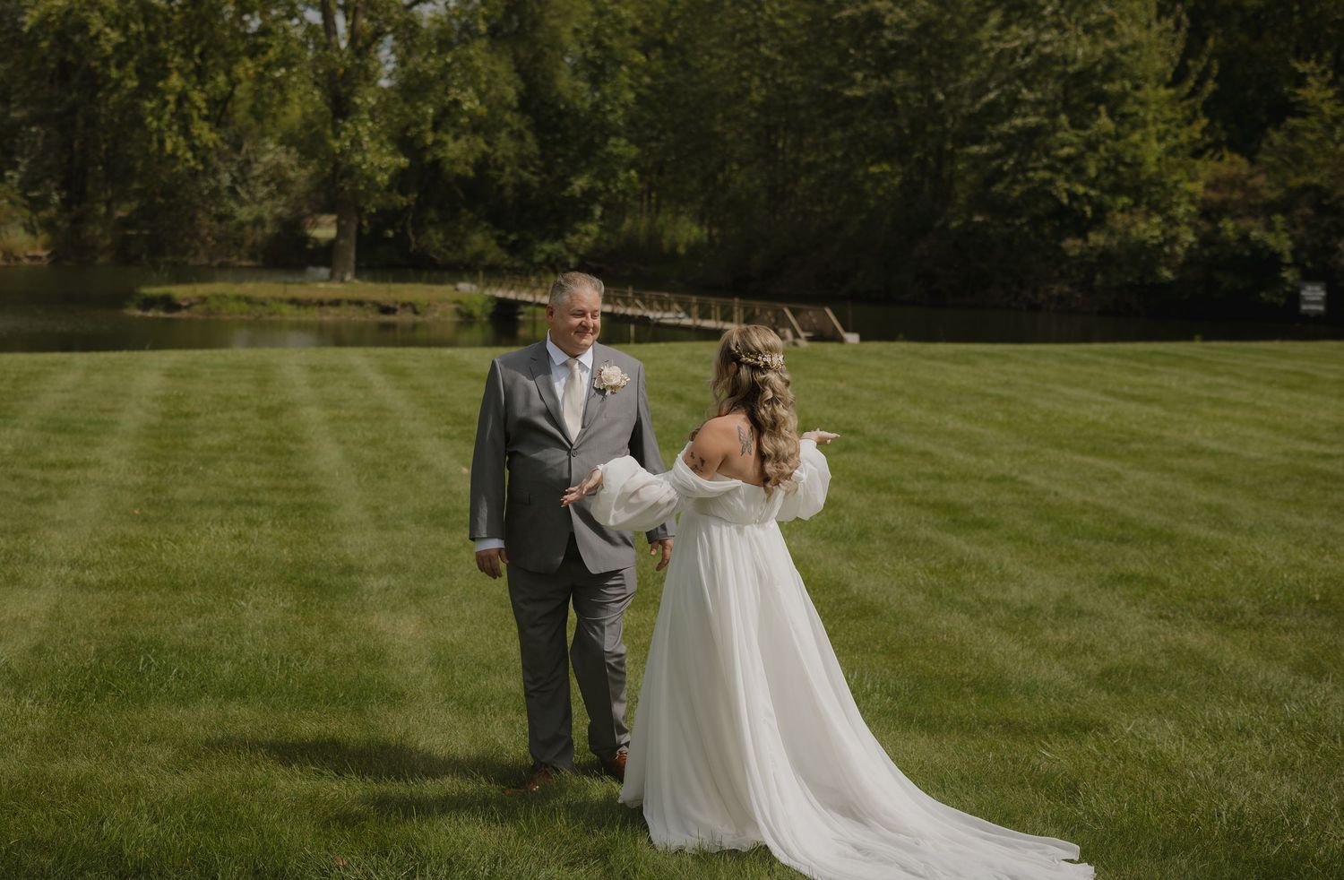 Wedding party members in emerald green dresses and gray suits pose together on a lush green lawn.