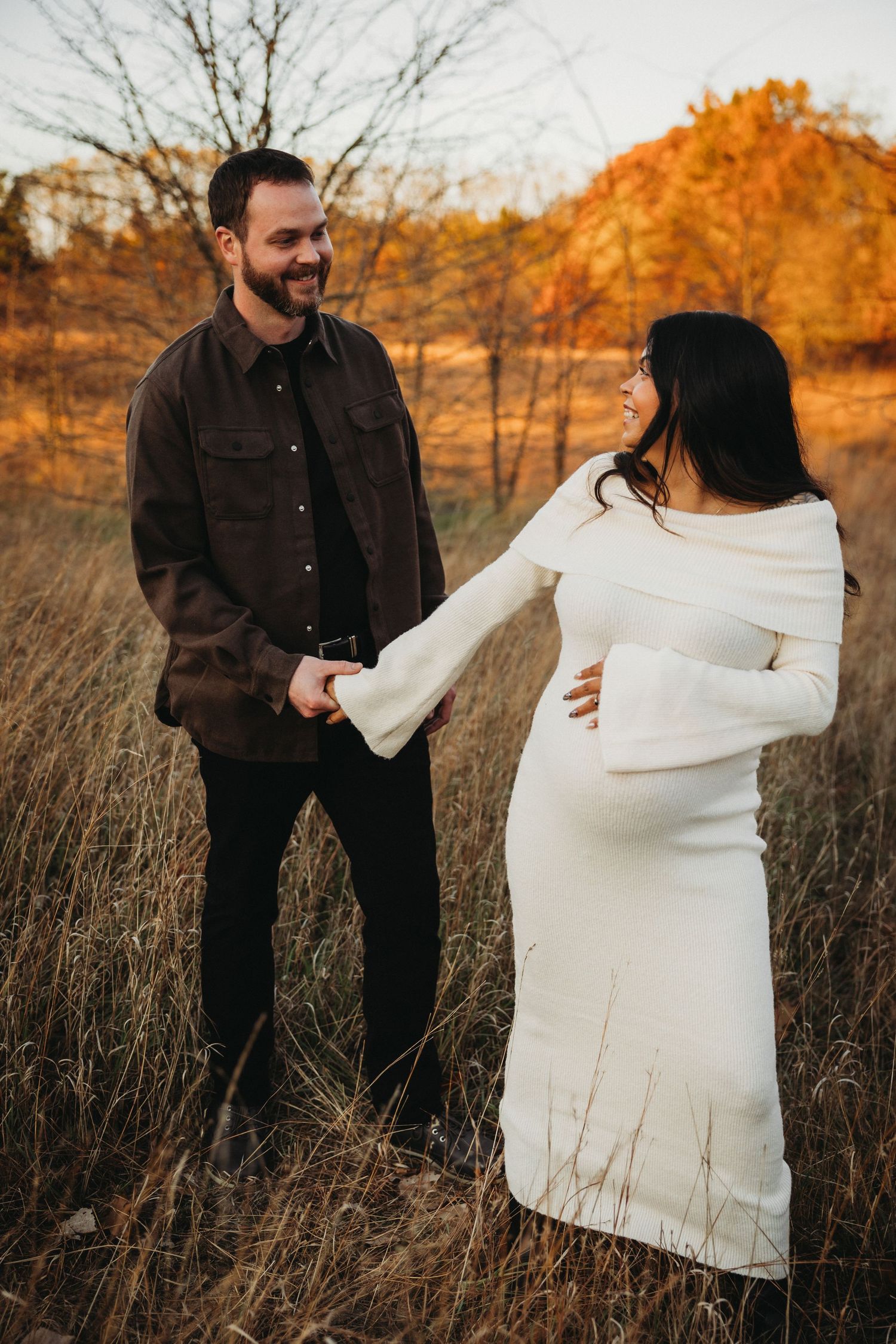 Couple holding hands in autumn field with warm sunset lighting.