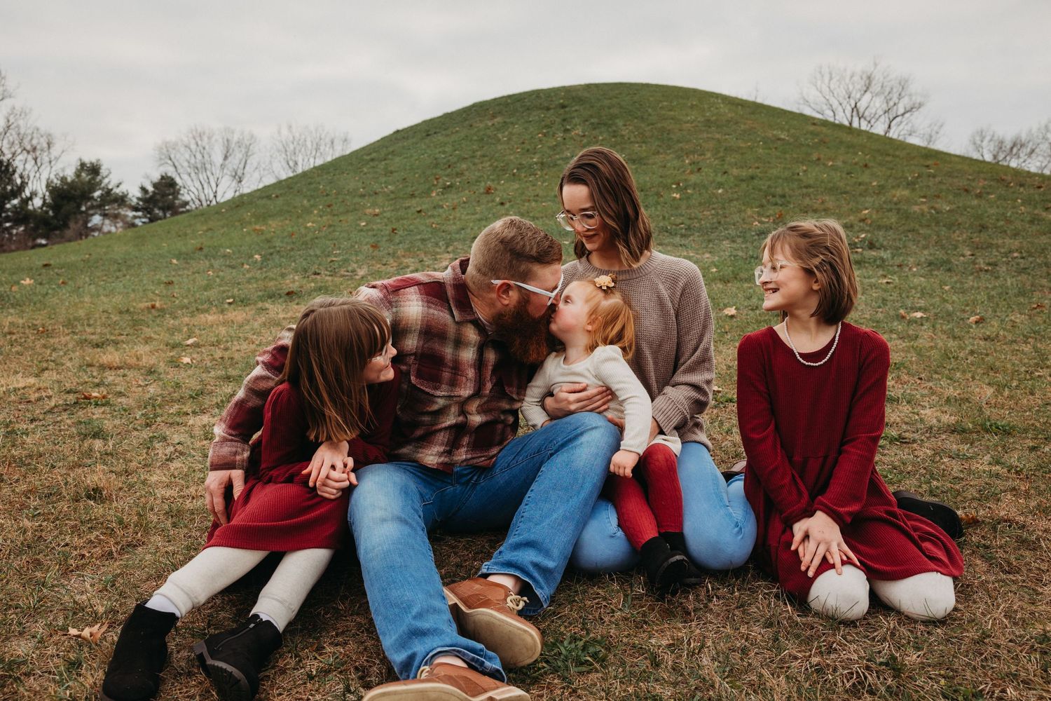 Candid moment of a family relaxing together on a grassy hillside during golden hour.