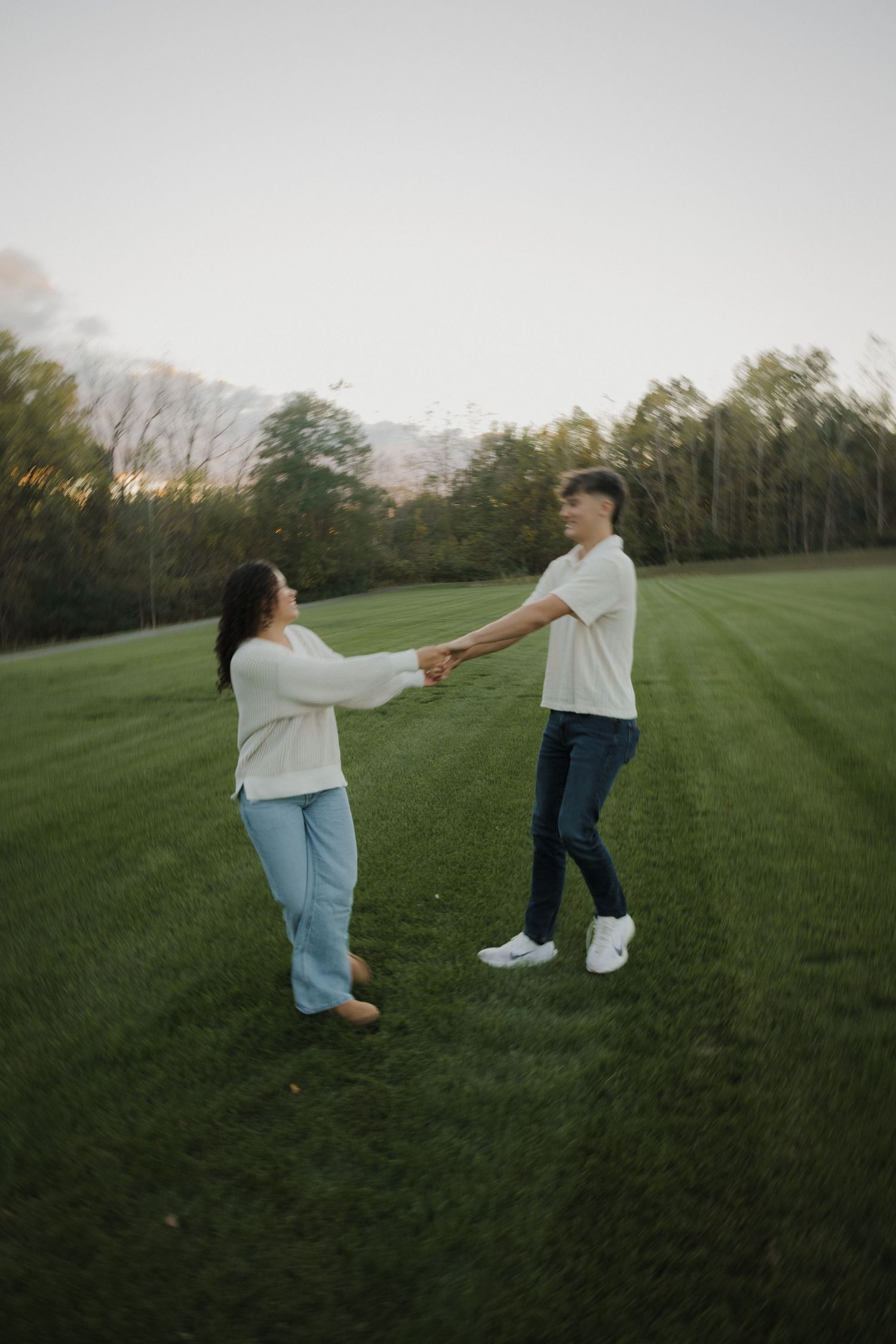 A playful couple dances and spins together on a vast green lawn at sunset.