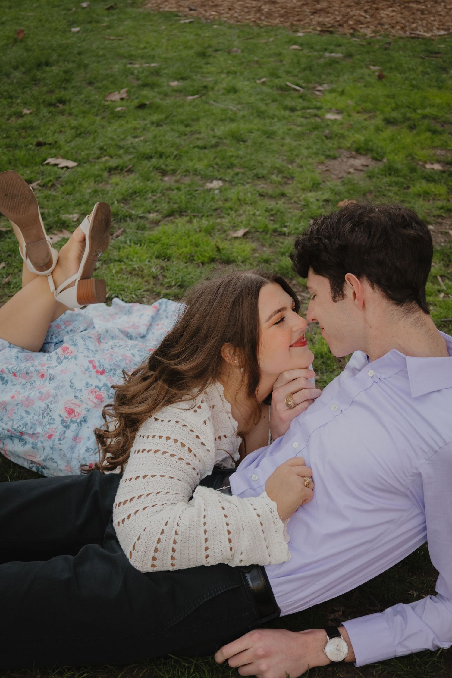 Romantic couple lying on grass in a park, sharing a tender moment with a flower between them.