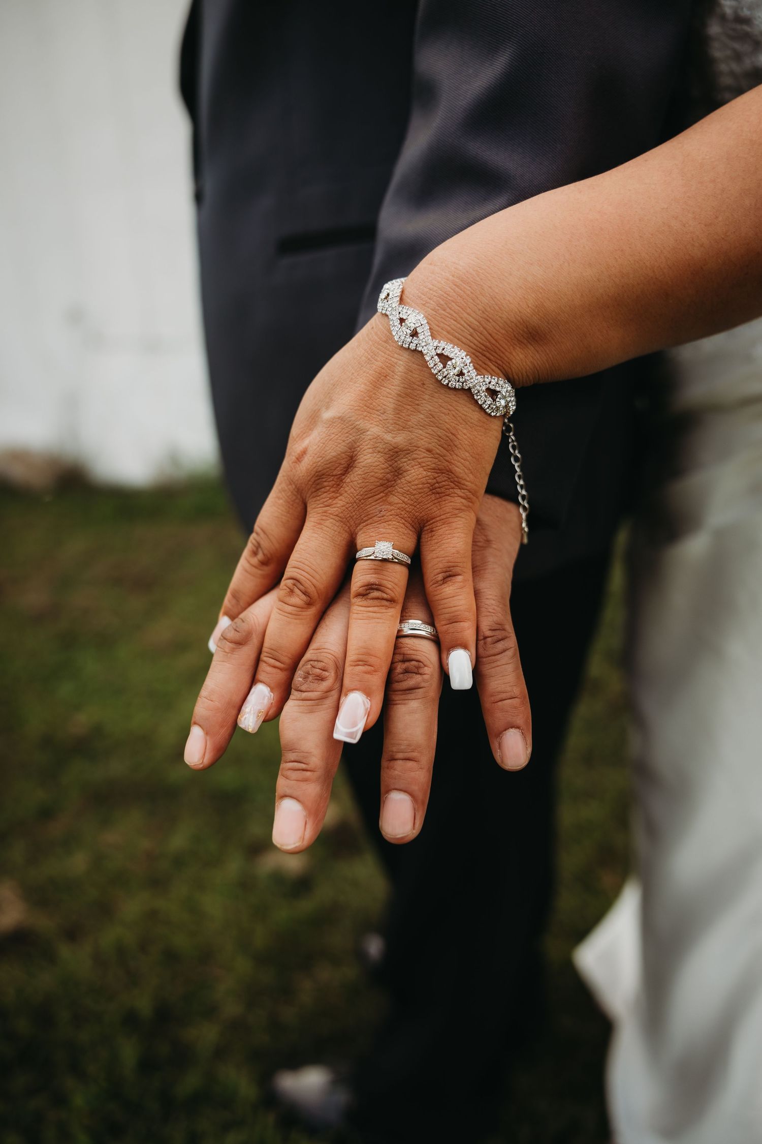 Close-up of hands showing wedding rings and a delicate silver bracelet against formal attire.