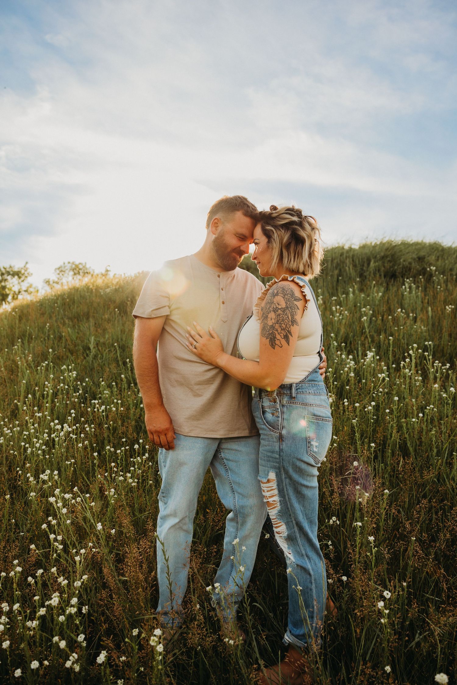 Romantic couple embracing in a wildflower meadow during golden hour sunset.