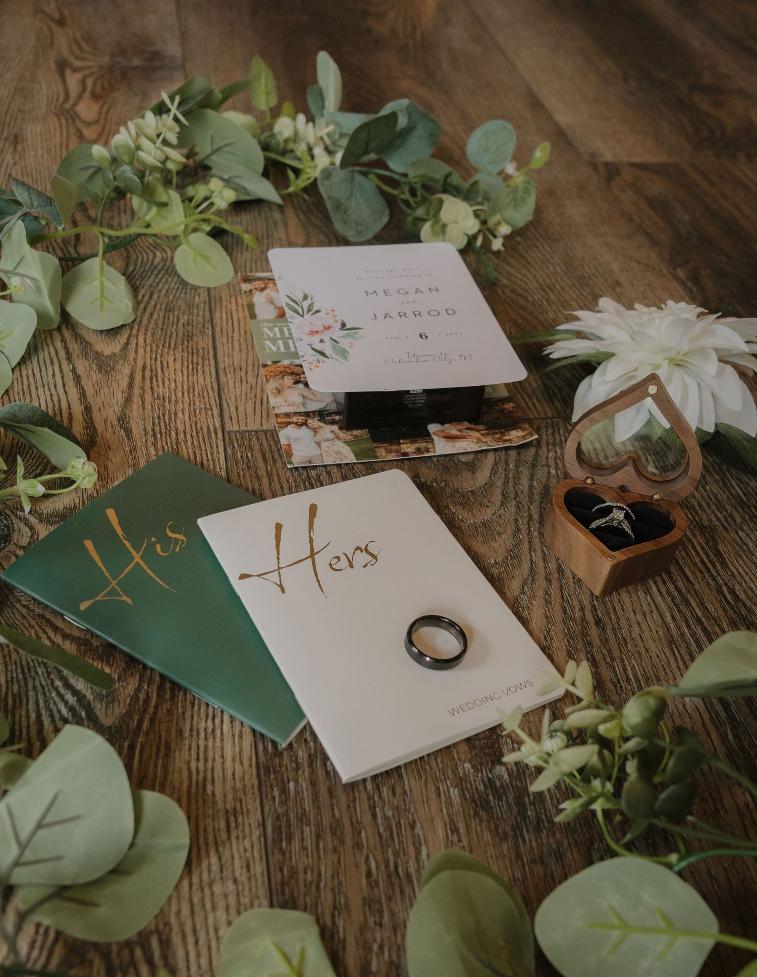 Wedding place cards and greenery decorations arranged on rustic wooden table.