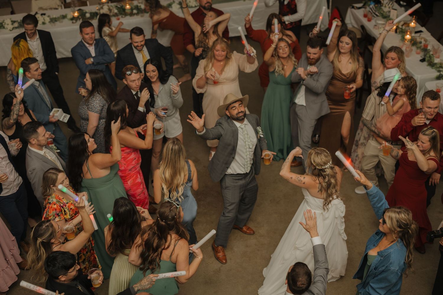 Large group of wedding guests dancing and celebrating at indoor reception.