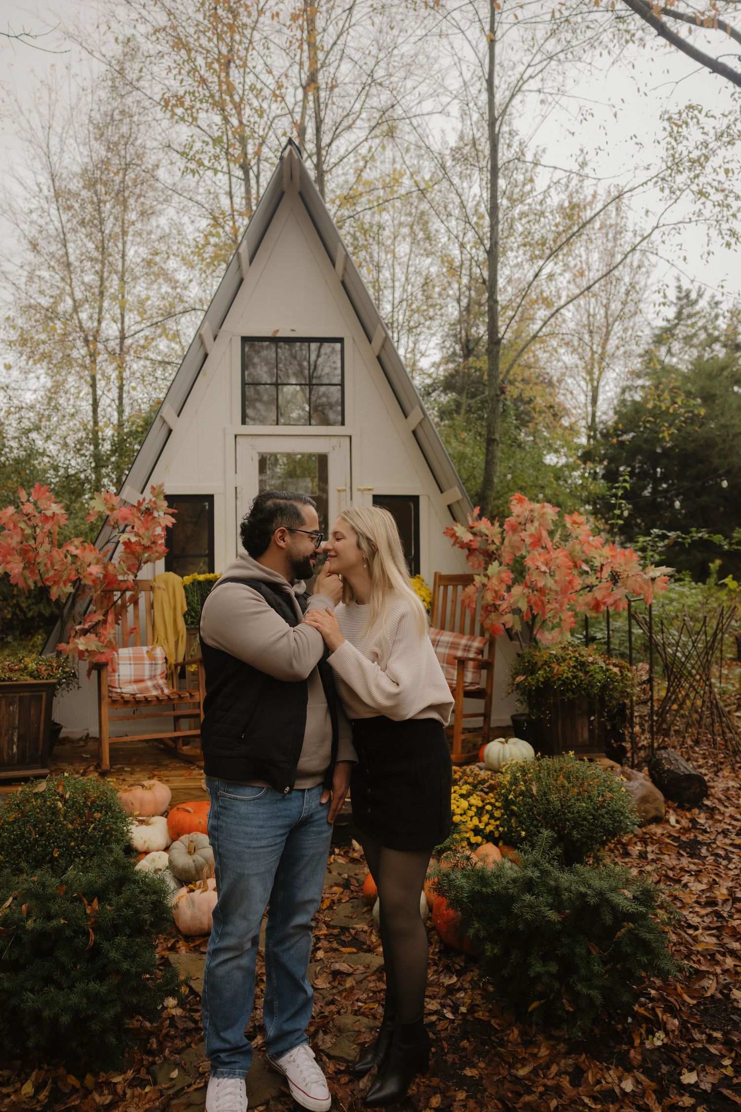 A romantic fall photoshoot set against a white A-frame structure with autumn foliage and pumpkins.