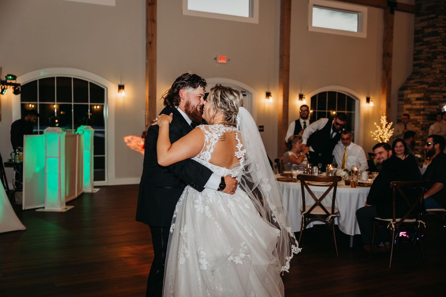 First dance in elegant reception hall with arched windows and ambient lighting.