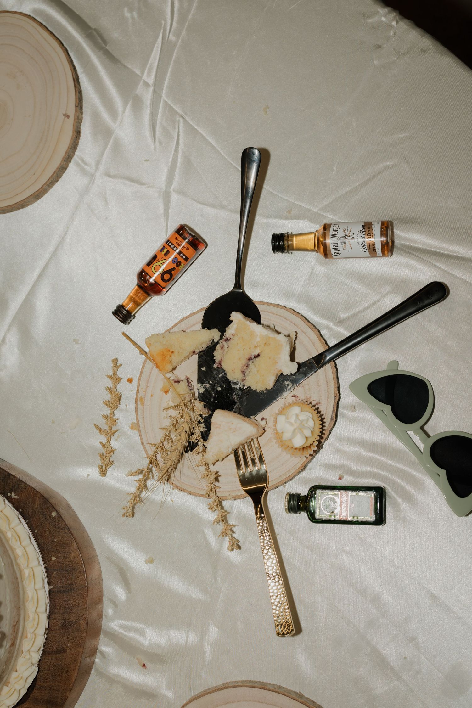 Overhead view of a cheese board with utensils, mini liquor bottles, and decorative elements on a white tablecloth.