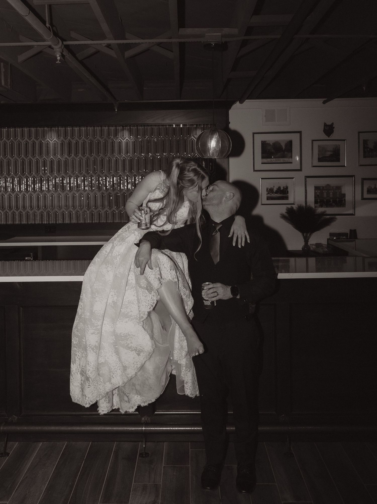 Black and white photo of a bride and groom sharing a romantic kiss at a bar during their wedding reception.