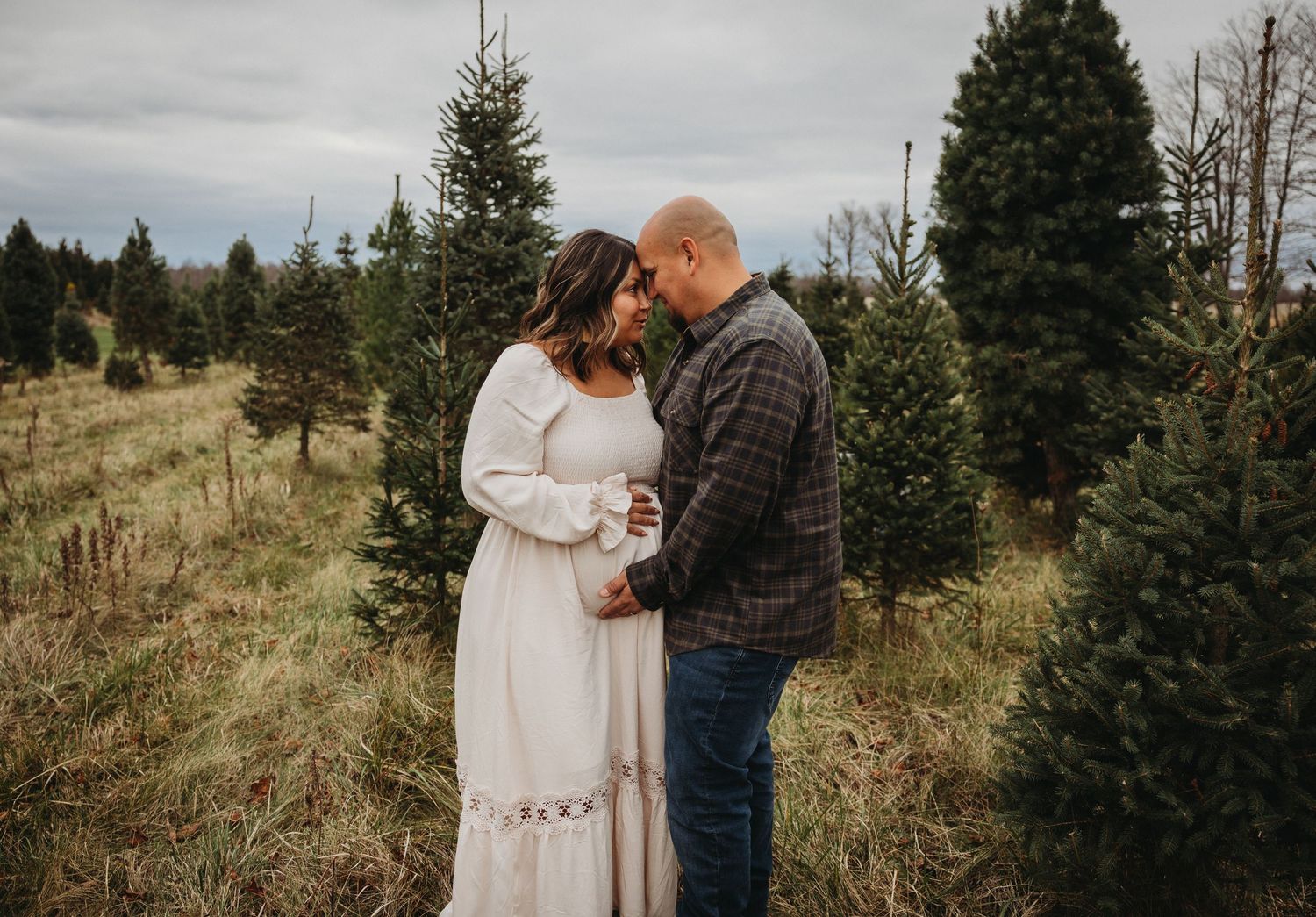 Intimate couple embracing in white dress and plaid shirt among evergreen trees on misty mountainside.