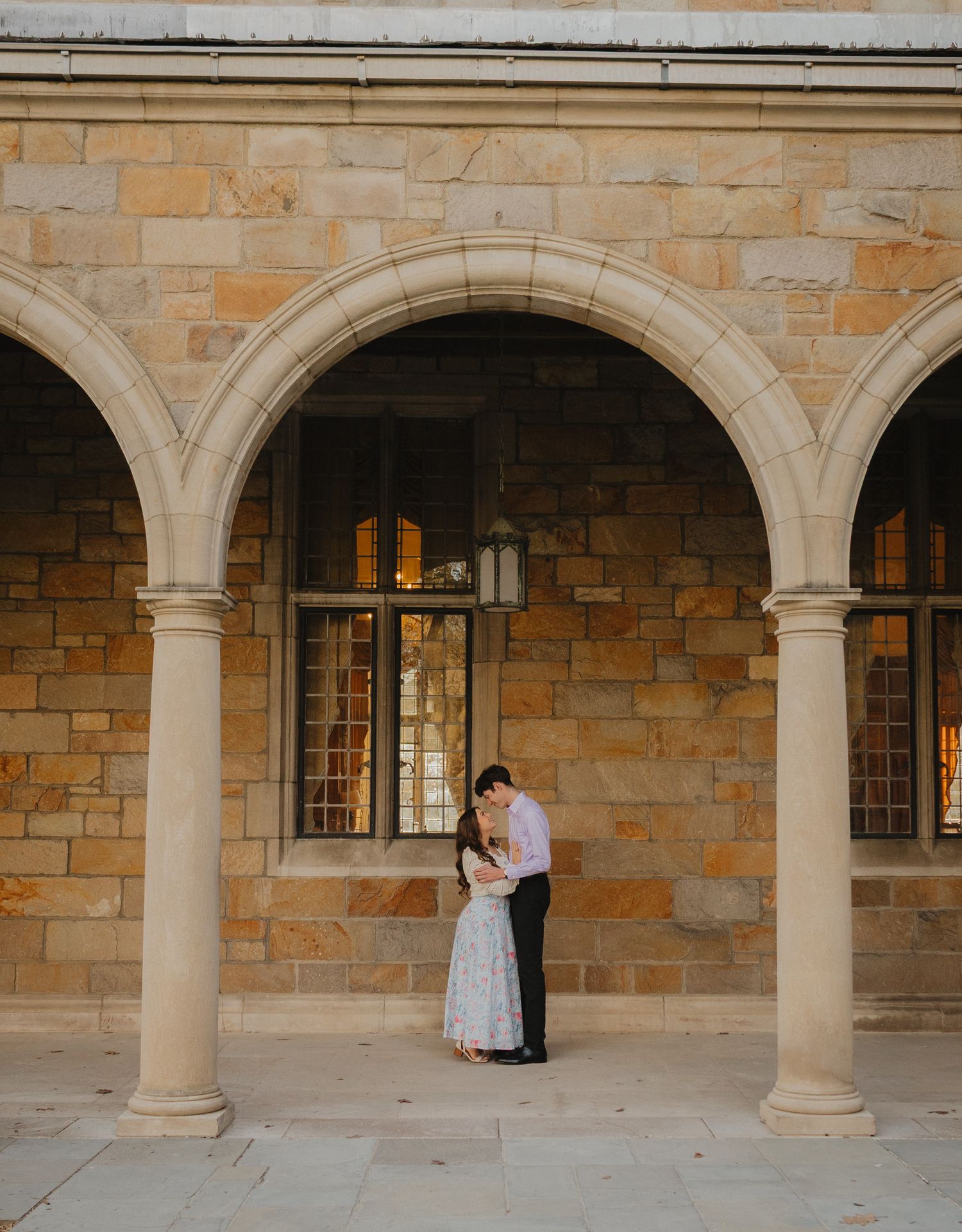 Couple embracing under stone arches of a historic building during golden hour engagement photo session.
