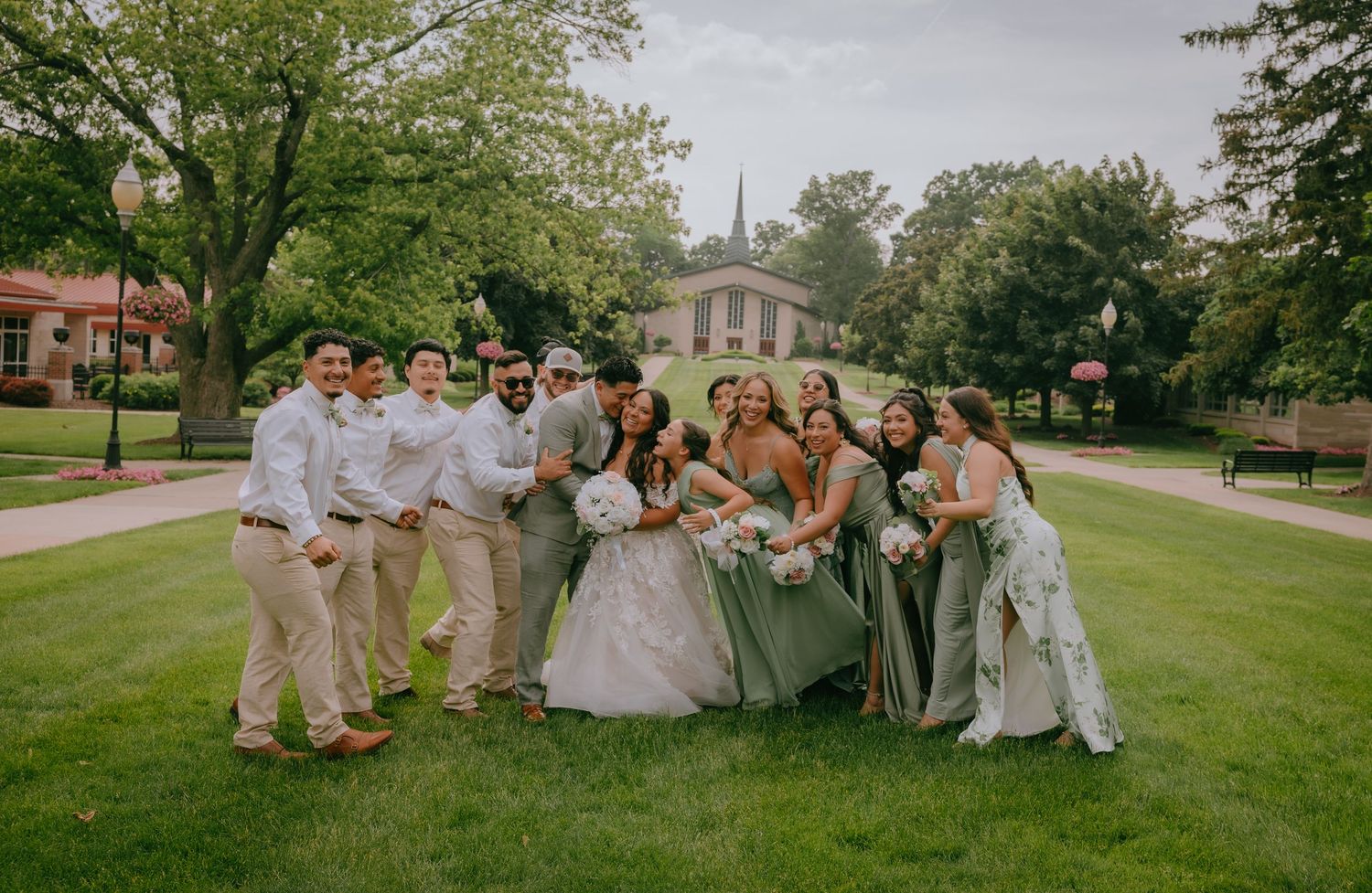 Wedding party in formal attire posing together on a sunny day with a church steeple visible in the background.